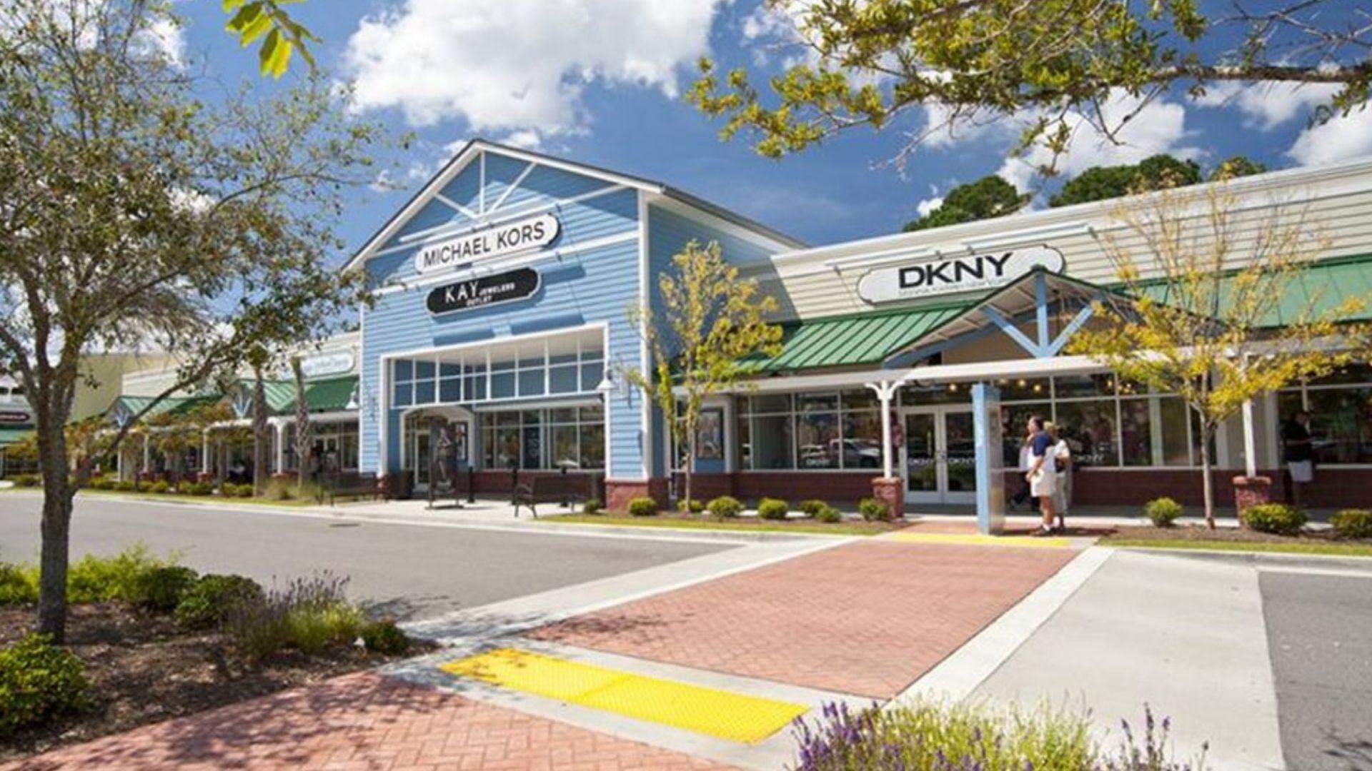 Outdoor outlet mall with Michael Kors, DKNY, Kay stores, brick crosswalks, trees and blue sky