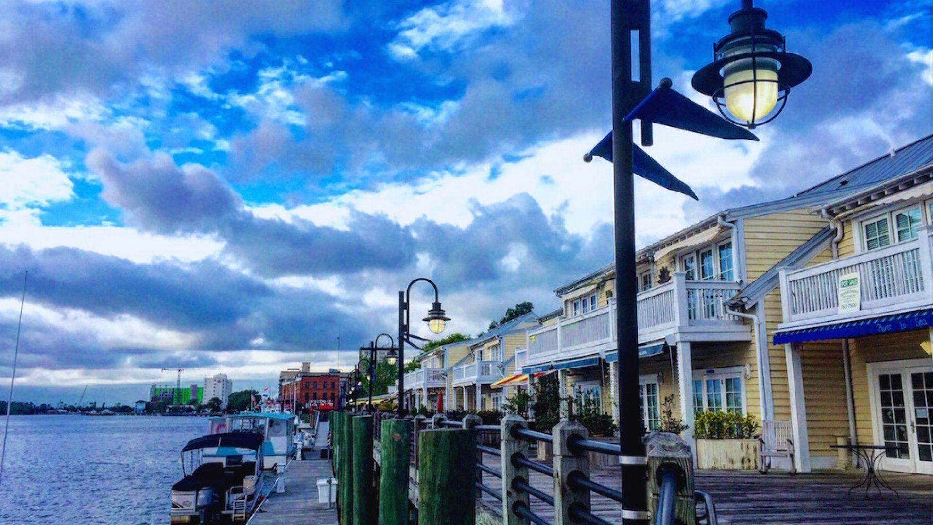 Sky over Wilmington Riverwalk with vintage lamps docked boats and yellow waterfront shops lining the boardwalk.