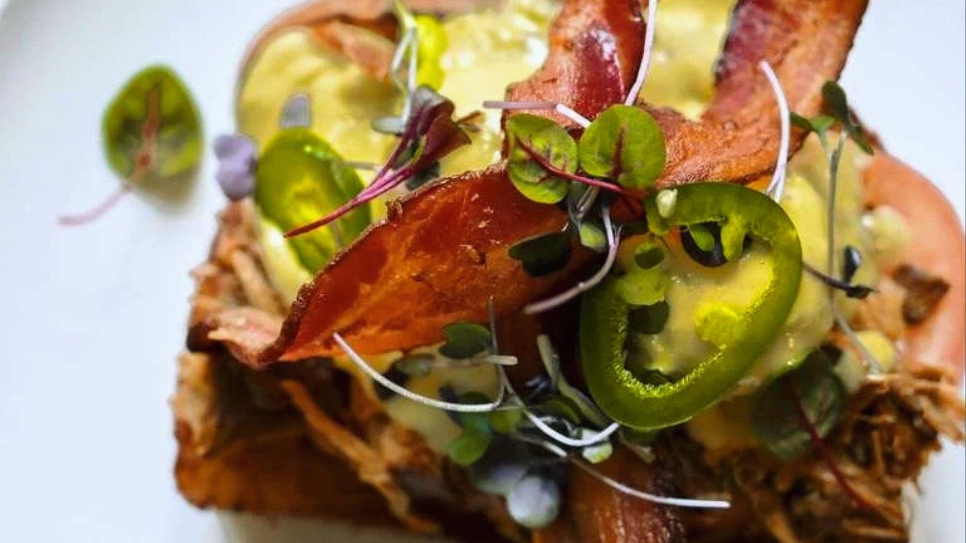 Gourmet pulled pork toast topped with crispy bacon, jalapeño slices, microgreens and creamy sauce