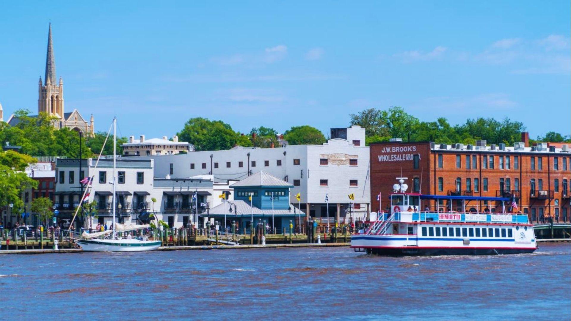 Riverfront view of Wilmington with tour boat Henrietta sailboat docked and historic church steeple background.