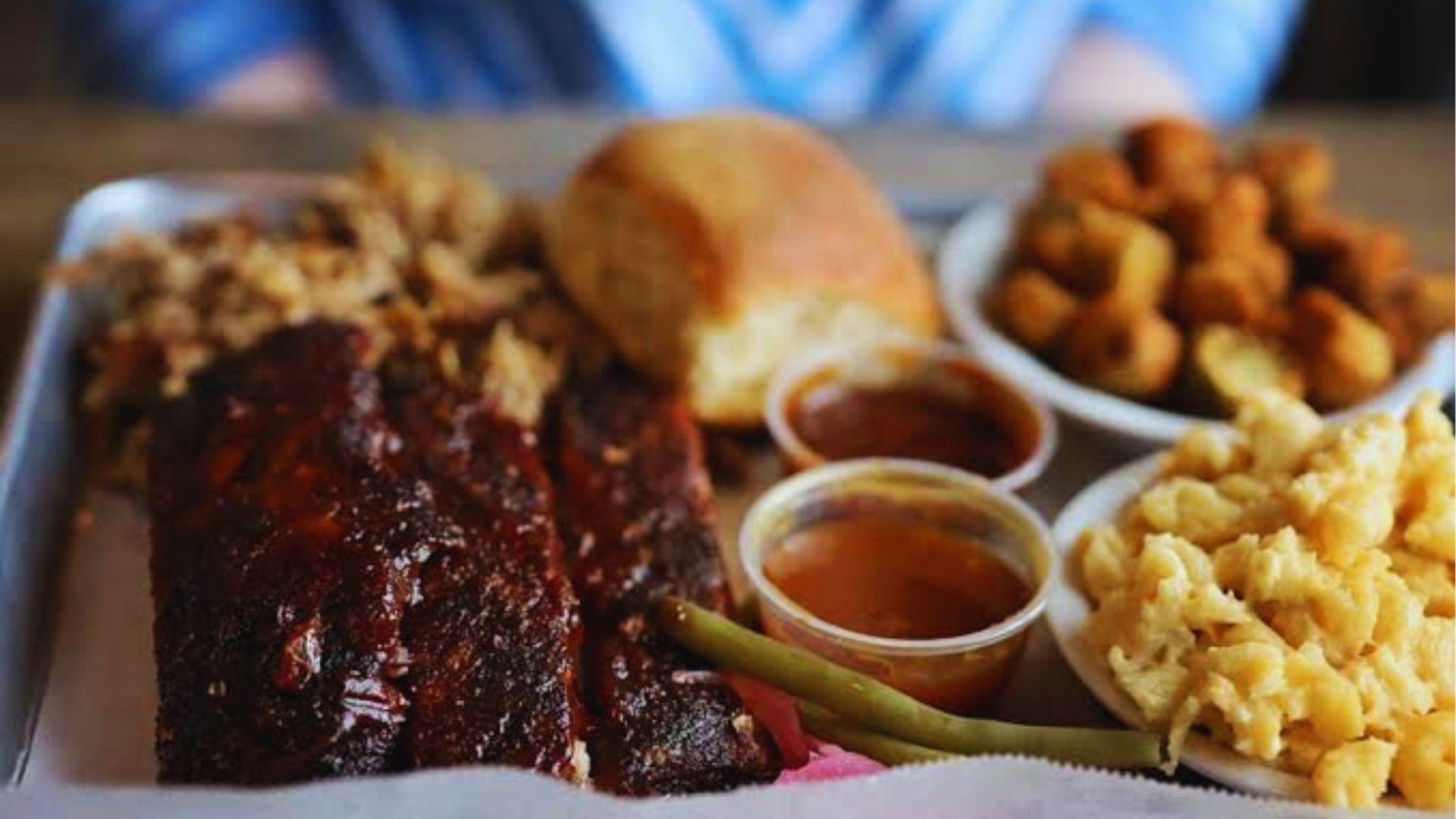 Delicious barbecue platter with glazed ribs pulled pork macaroni cheese fried okra bread and sauces.