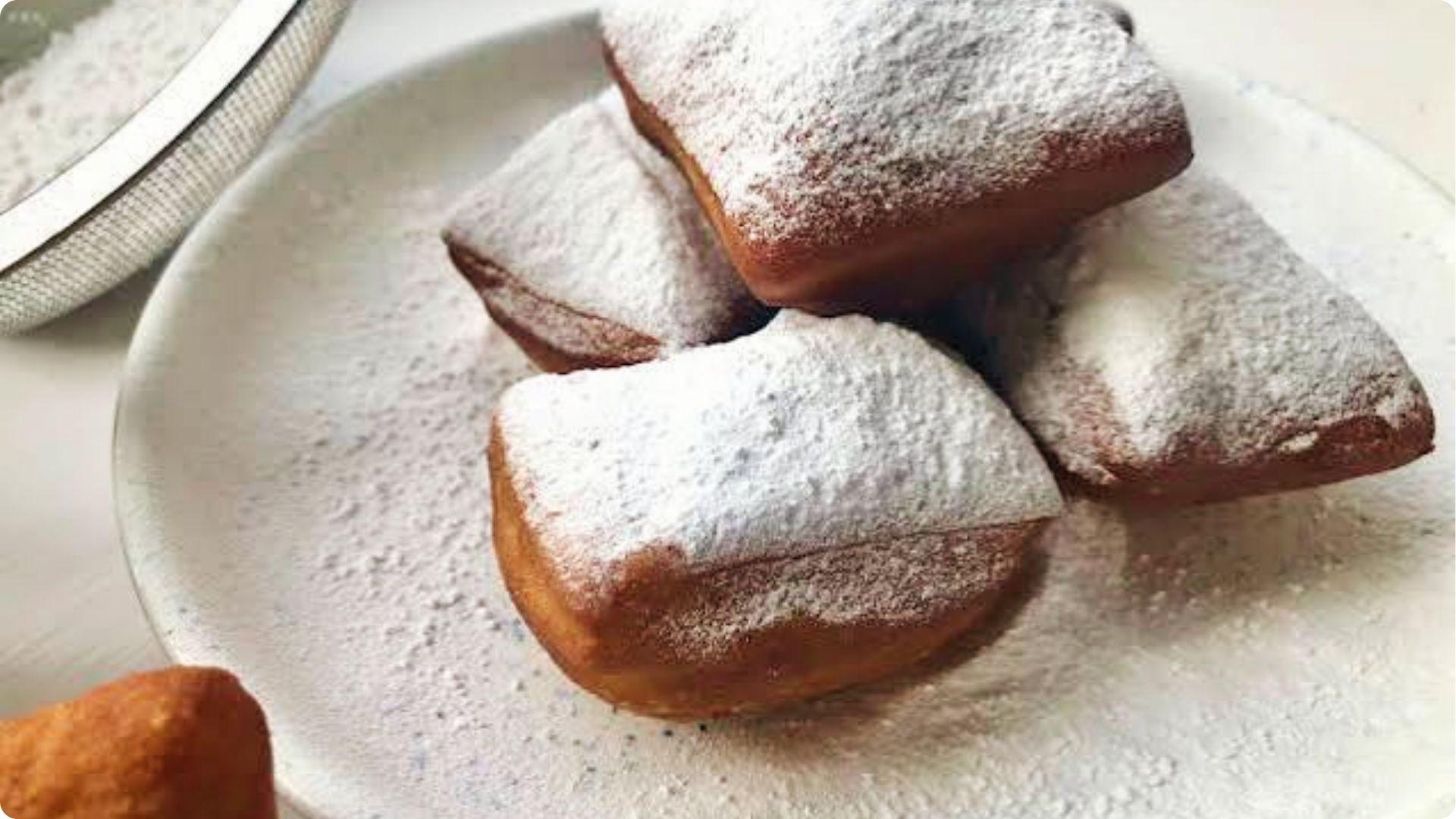 Fresh powdered sugar beignets stacked on white plate, famous sweet treat at French Quarter cafes