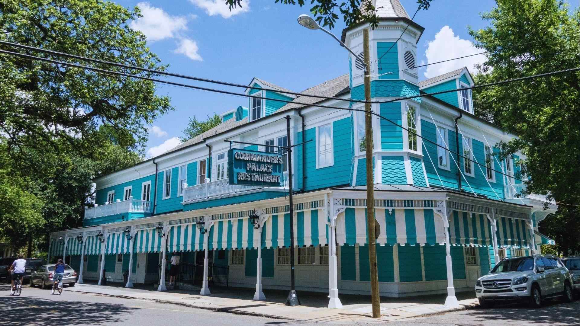 Turquoise Commander's Palace Restaurant building with striped awnings turret and street view on a sunny day.