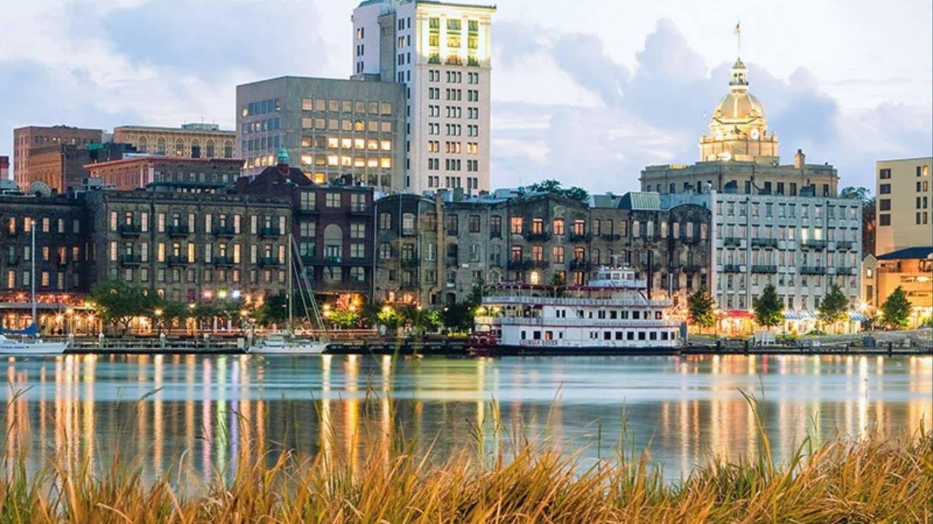Savannah riverfront at dusk with illuminated historic buildings reflecting on calm water