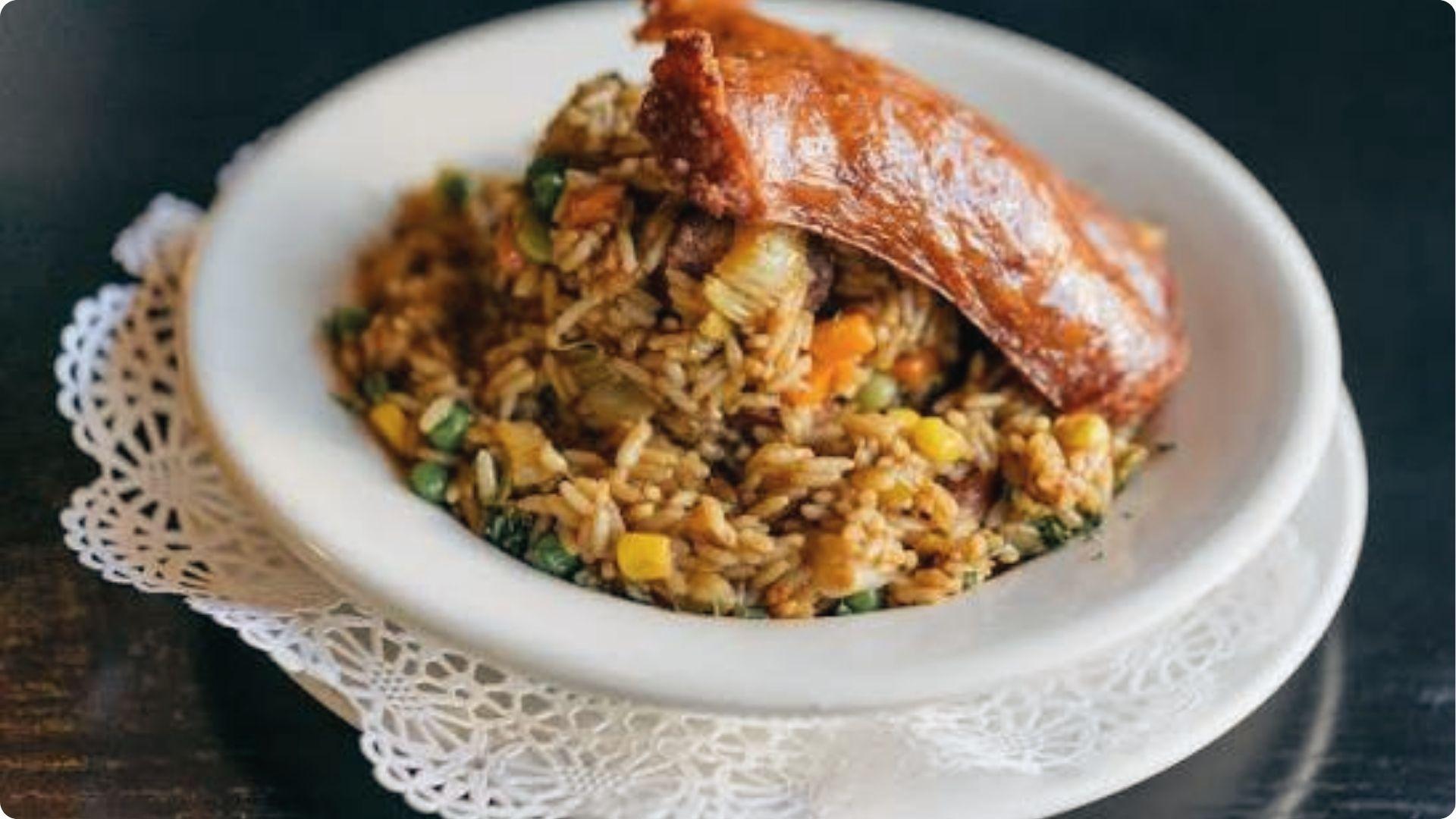 New Orleans dirty rice with veggies and crispy fried pork chop served in white bowl on doily.