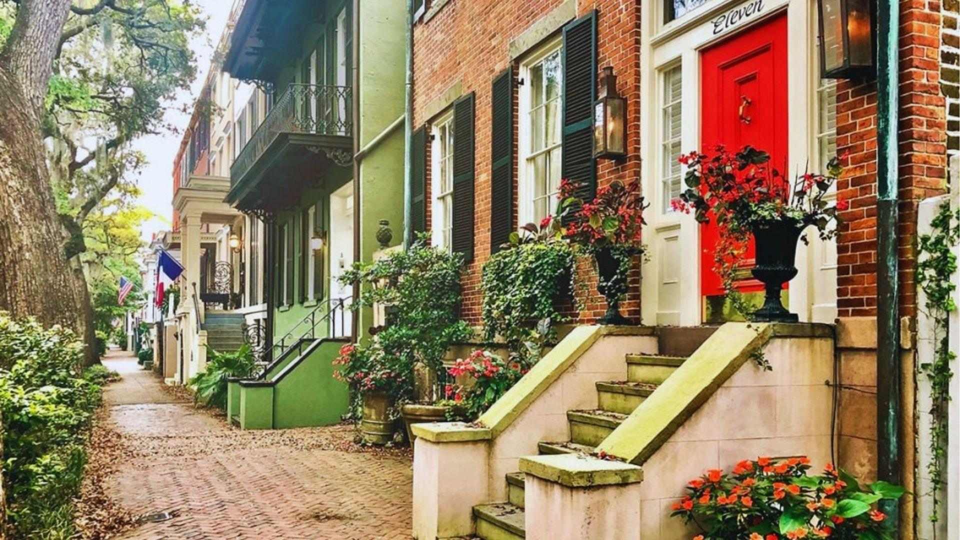 Historic Savannah row houses with bright red door flower planters along charming brick sidewalk pathways.