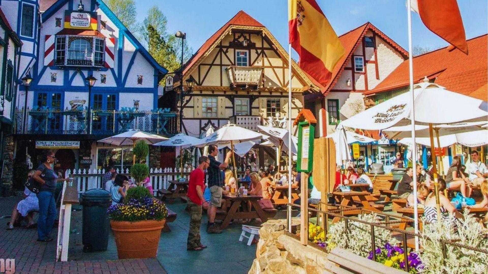 Outdoor patio of Old Heidelberg German Restaurant with Bavarian buildings, picnic tables and umbrella shades.