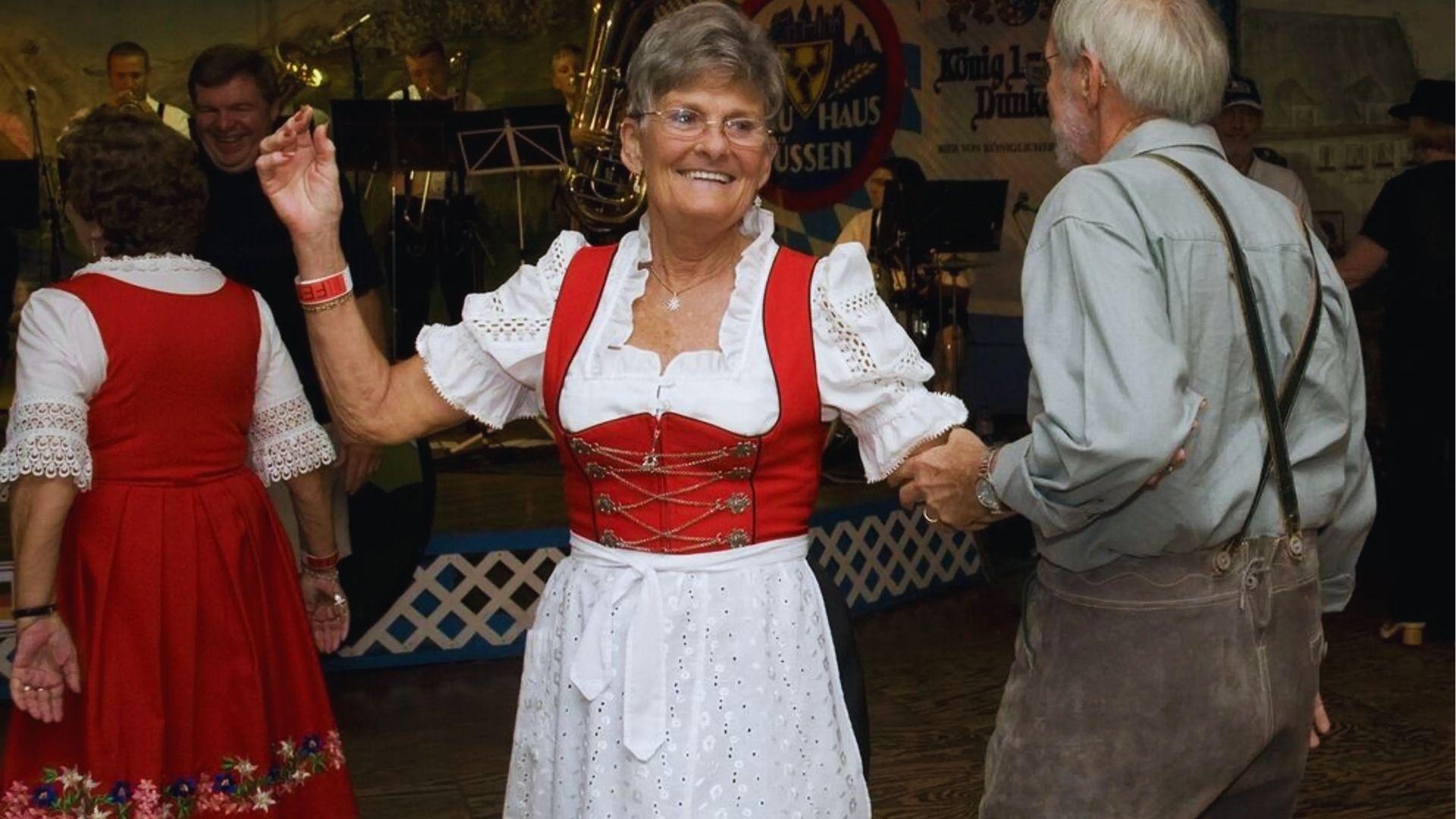 Woman in red and white dirndl dancing with man at indoor Oktoberfest celebration with band.