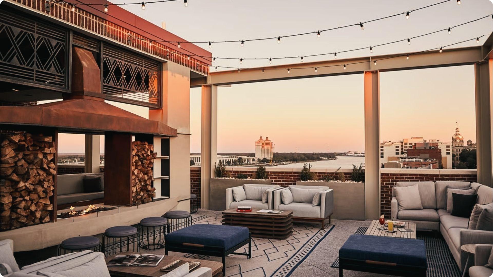 Rooftop happy hour venue at sunset with fireplace, string lights and Savannah riverfront views