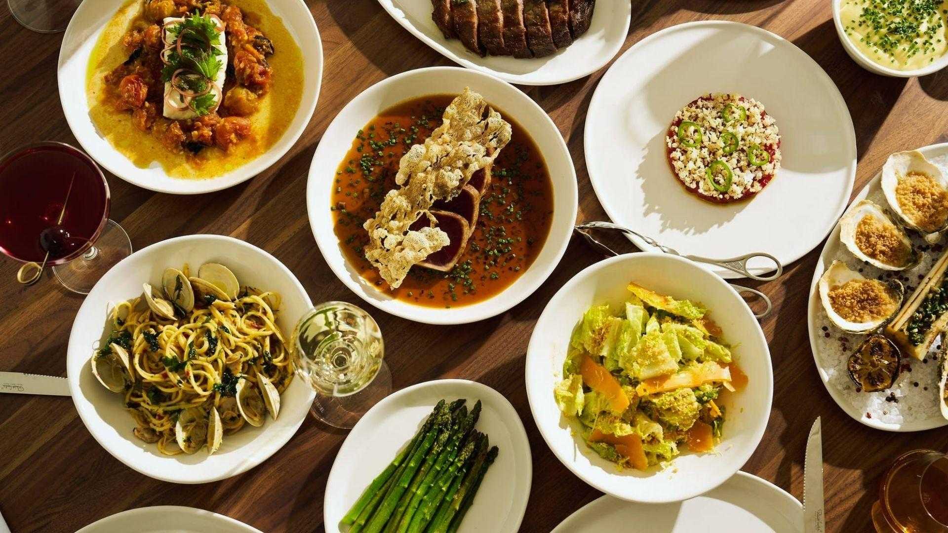 Overhead spread of steak, seared tuna, beef tartare, baked oysters, clam pasta and asparagus