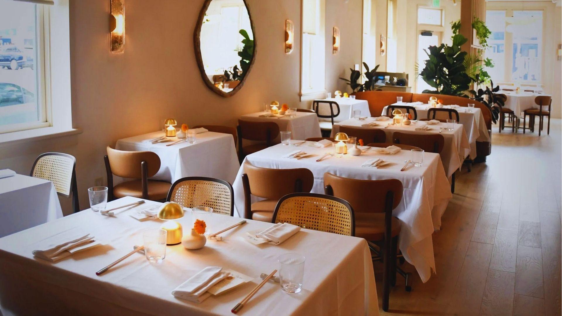 Bright elegant restaurant interior with white tablecloths, gold dome lamps and cane chairs in sunlight.