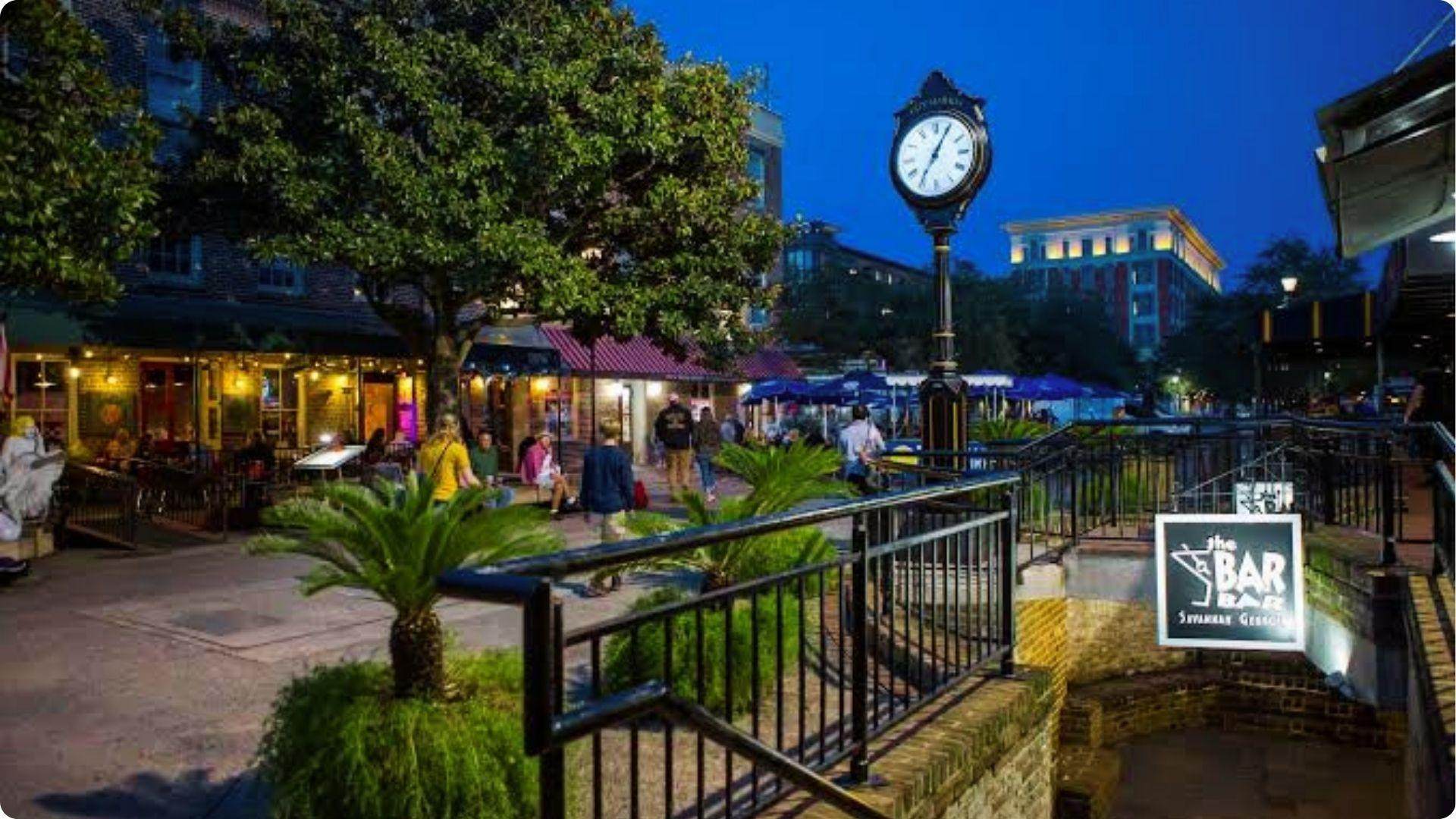 Night view of Savannah City Market clock with lively restaurants on self-guided walking tour stop.