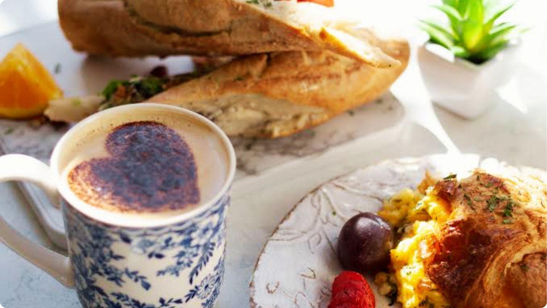 Heart cocoa latte in floral mug with croissant and sandwich, best coffee Savannah breakfast spread