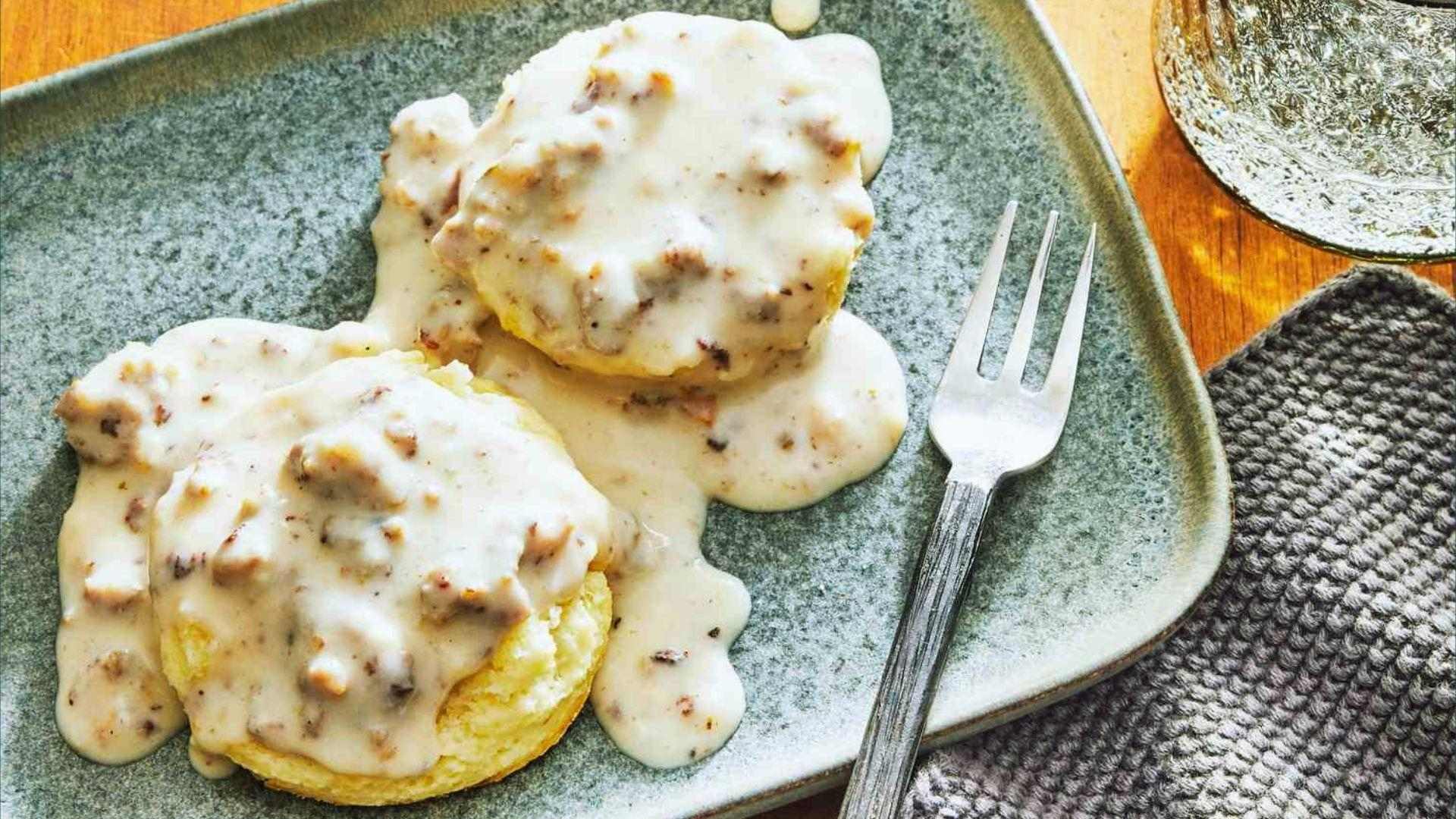 Fluffy biscuits smothered in creamy sausage gravy on gray plate with fork