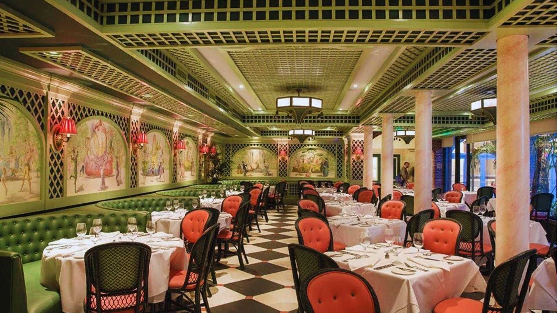 Elegant green lattice dining room with mural panels checkered floor coral chairs and white tablecloths.