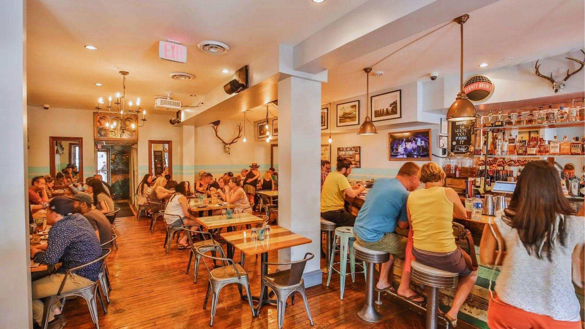 Casual bar restaurant filled with patrons dining at tables and bar stools under warm lighting.