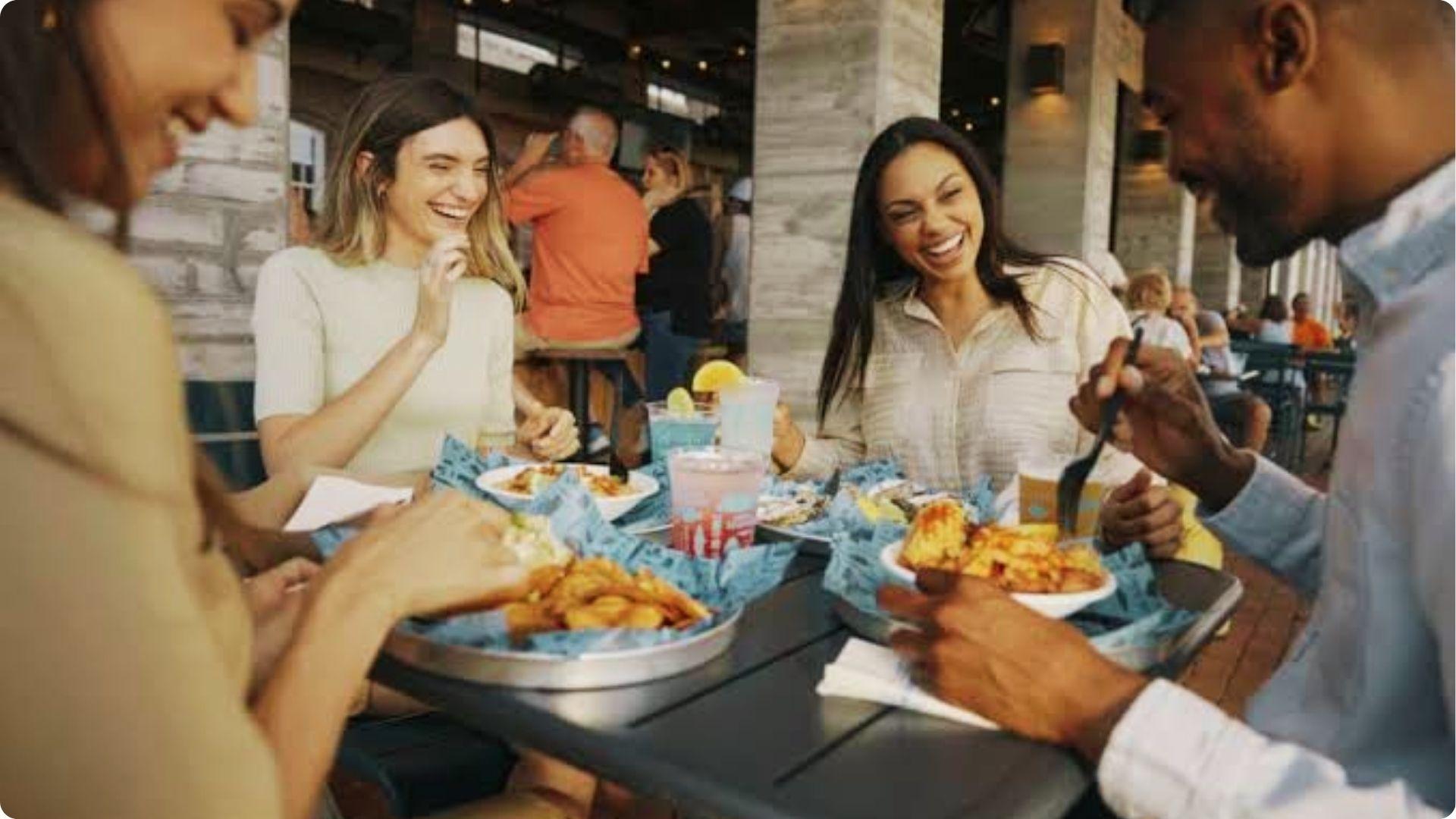 Friends laughing over fried seafood and drinks at outdoor happy hour in Savannah Georgia patio