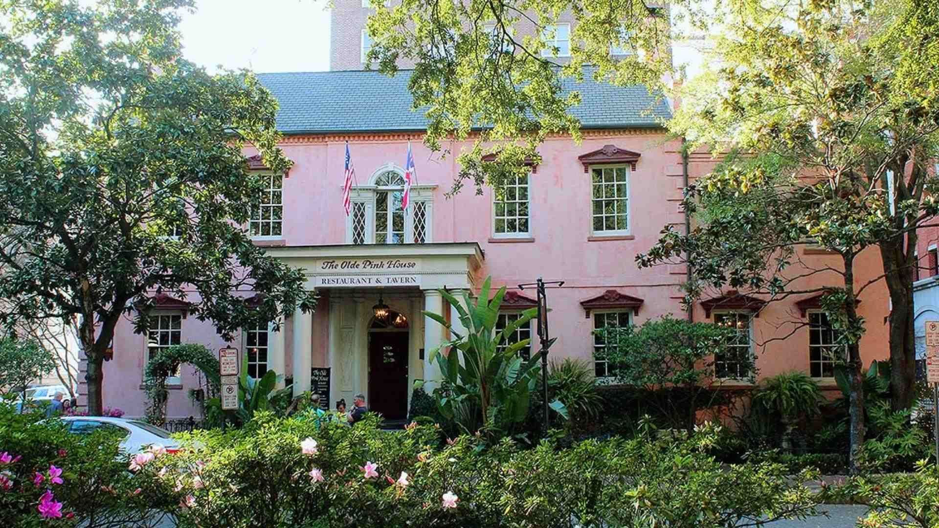 Pink historic building The Olde Pink House Restaurant & Tavern surrounded by green trees and flowering bushes.