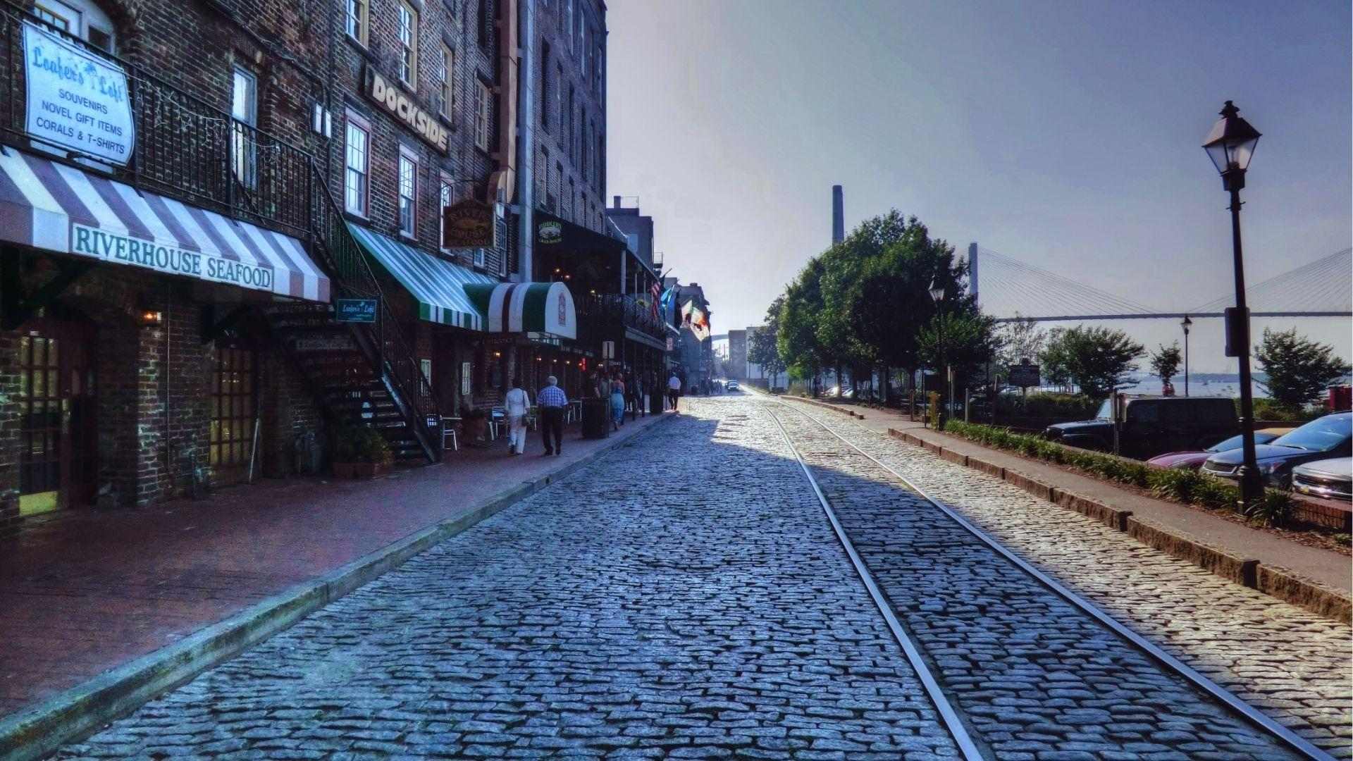 Cobblestone River Street with Riverhouse Seafood restaurant awnings train tracks leading toward Talmadge Bridge view.