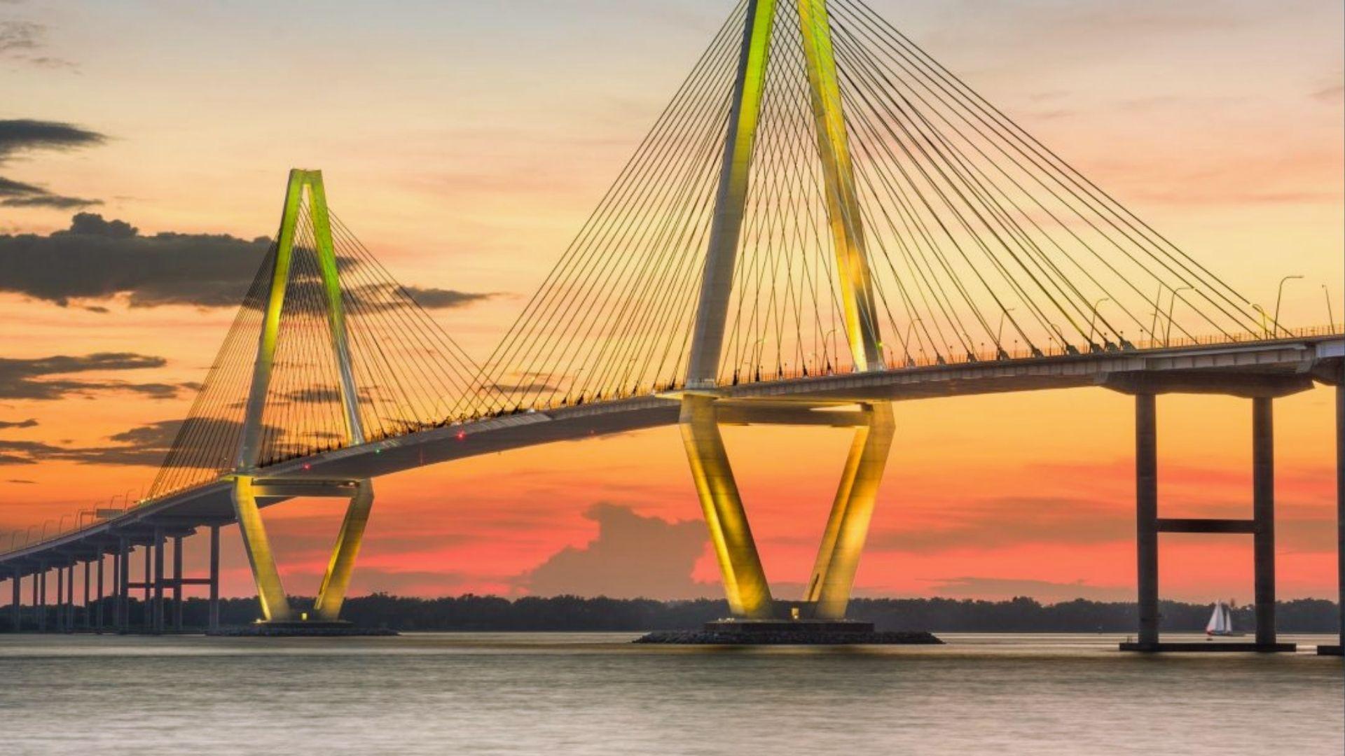 Arthur Ravenel Bridge glowing yellow at vibrant orange-pink sunset over water