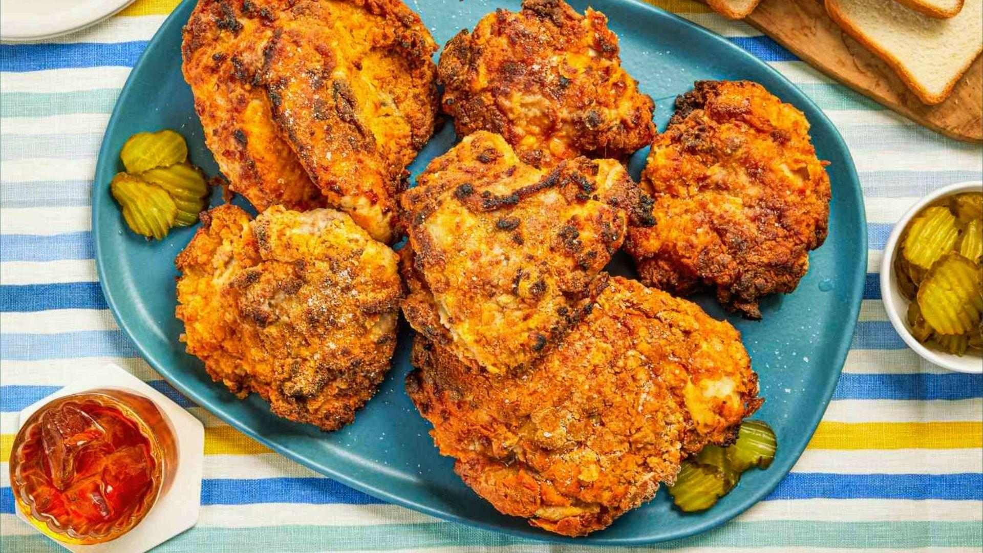 Crispy fried chicken thighs with pickle slices and iced tea on striped tablecloth