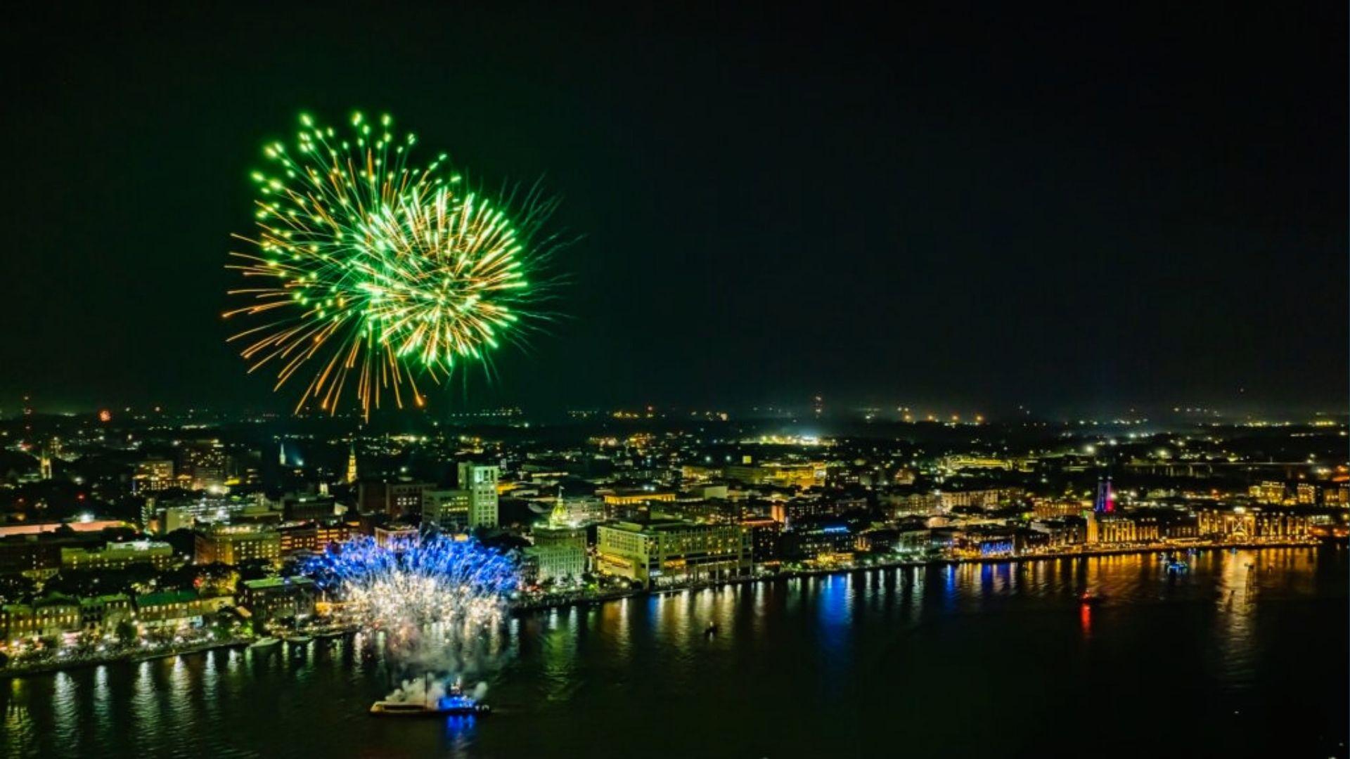Fireworks exploding in green and gold over Savannah skyline and river at night