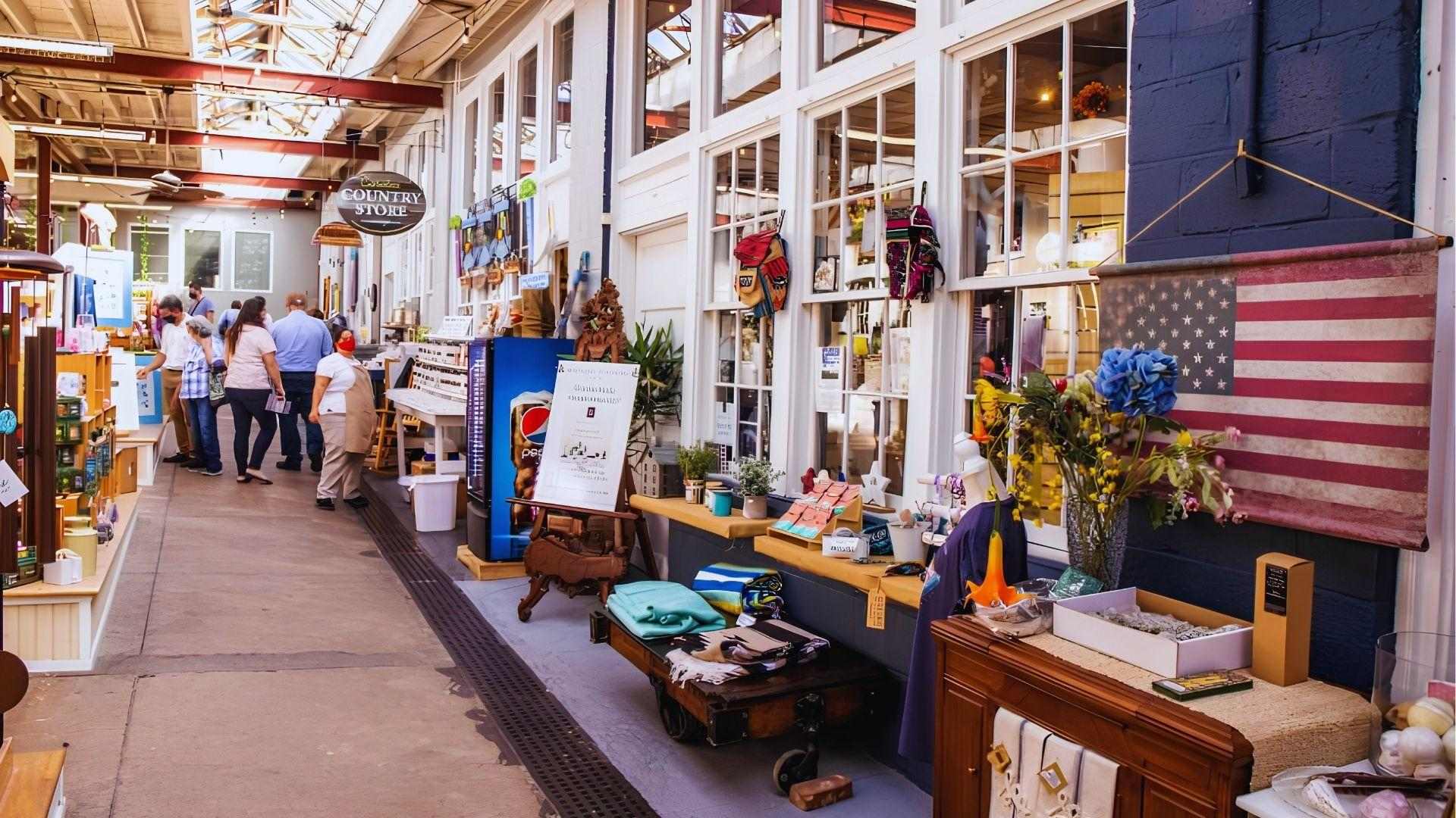 Indoor market with Country Store sign shoppers browsing colorful crafts, American flag and flowers displayed.