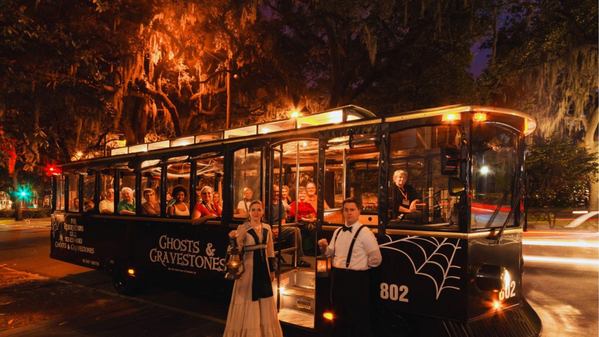 Ghost tour trolley at night with costumed guides holding lanterns under moss-draped oak trees glowing.