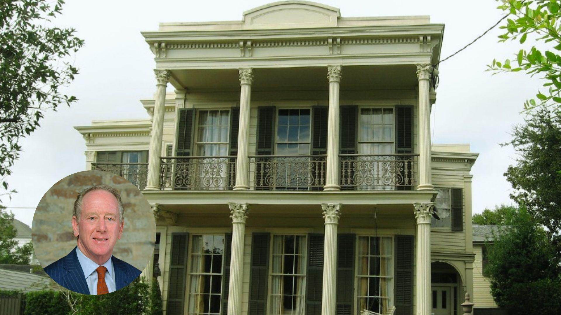 Two-story white historic mansion with tall Corinthian columns, ornate iron balcony, dark shutters, surrounded by greenery