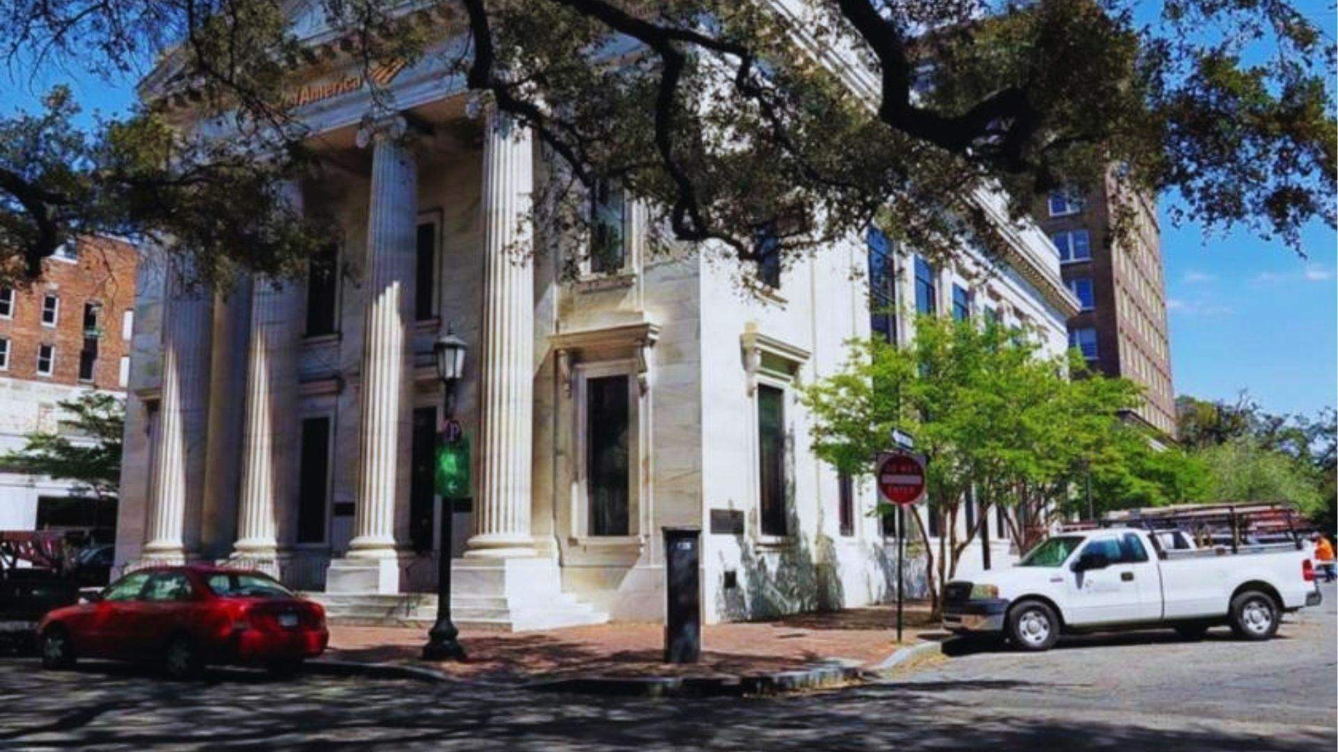 Neoclassical bank building with tall columns at Savannah intersection with red car and white truck.