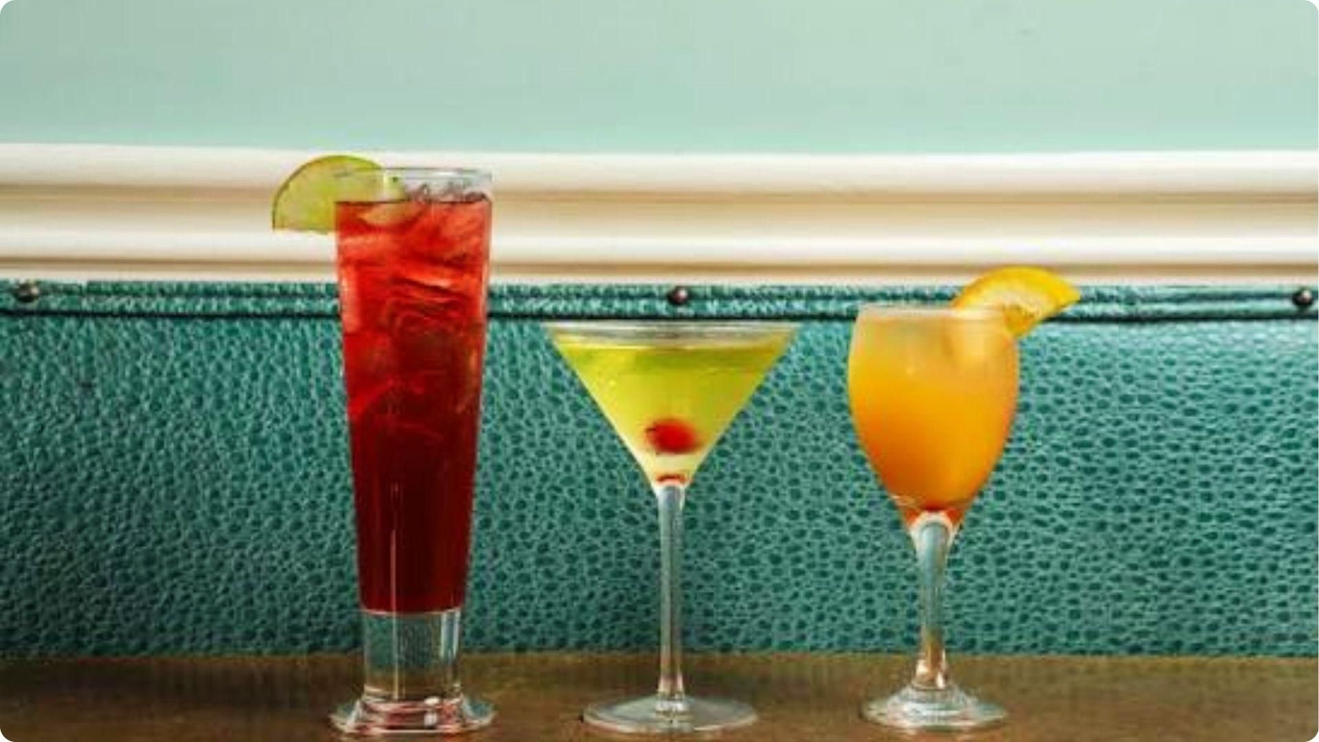 Three colorful classic New Orleans cocktails on bar table, must-try drinks on French Quarter bar crawl