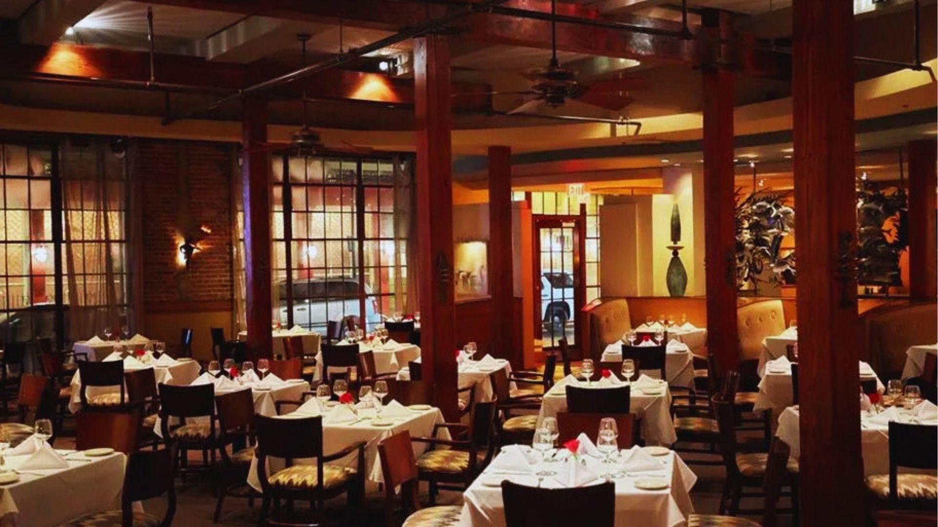 Dining room with brick walls white tablecloths, red roses and dark wooden pillars at night.
