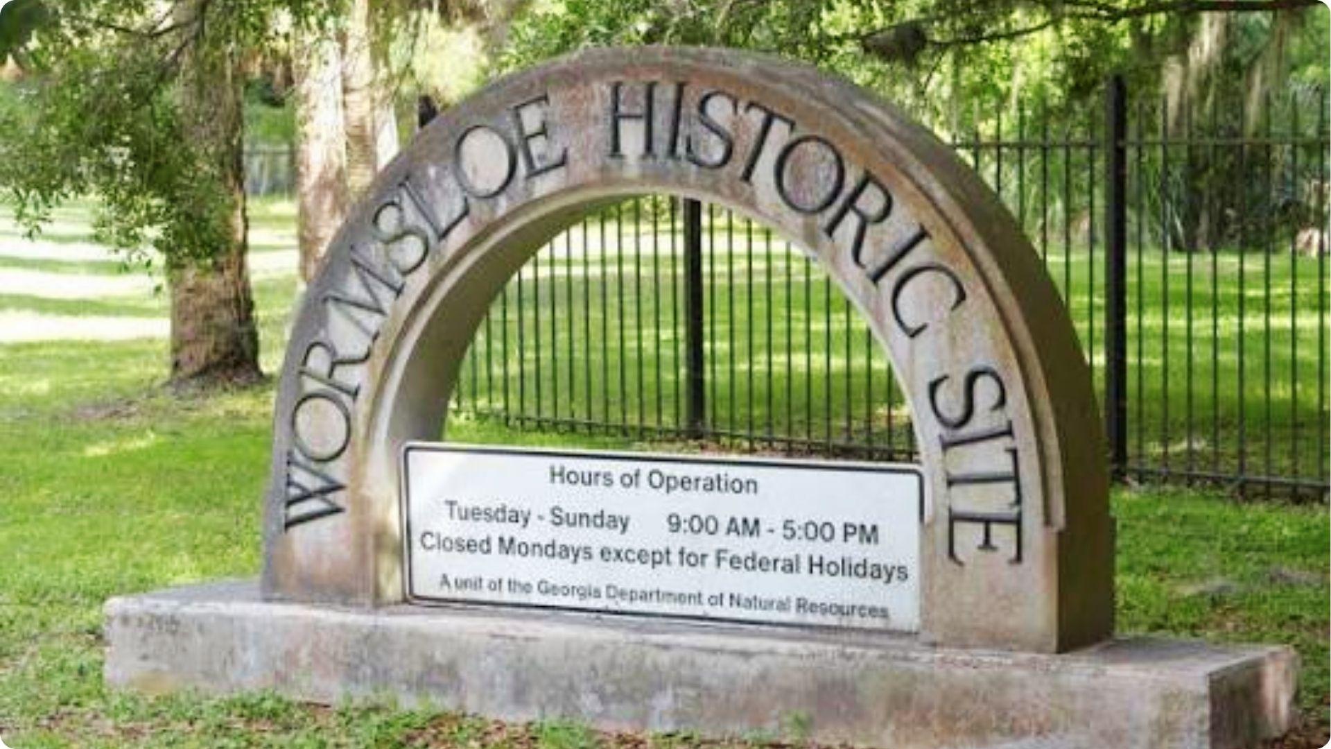 Stone arch entrance sign for Wormsloe Historic Site with hours displayed in Savannah Georgia