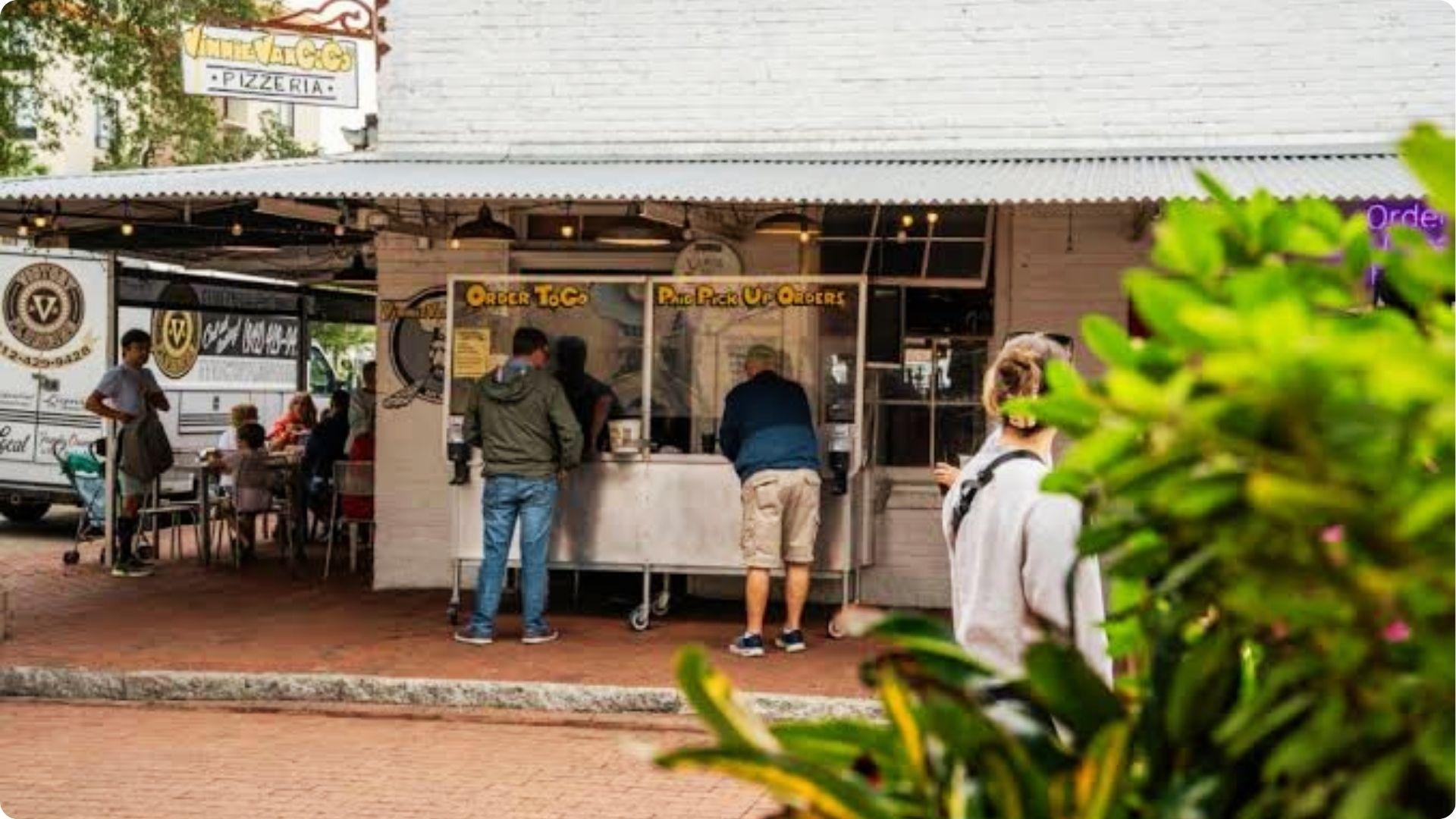 Guests ordering at Vinnie Van Go-Go Pizzeria takeout window in Savannah during casual happy hour