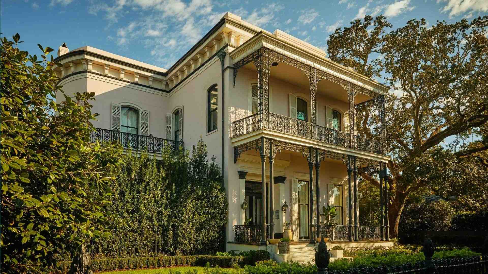 Pink Garden District mansion with ornate black iron double balconies, lush garden, sunny day