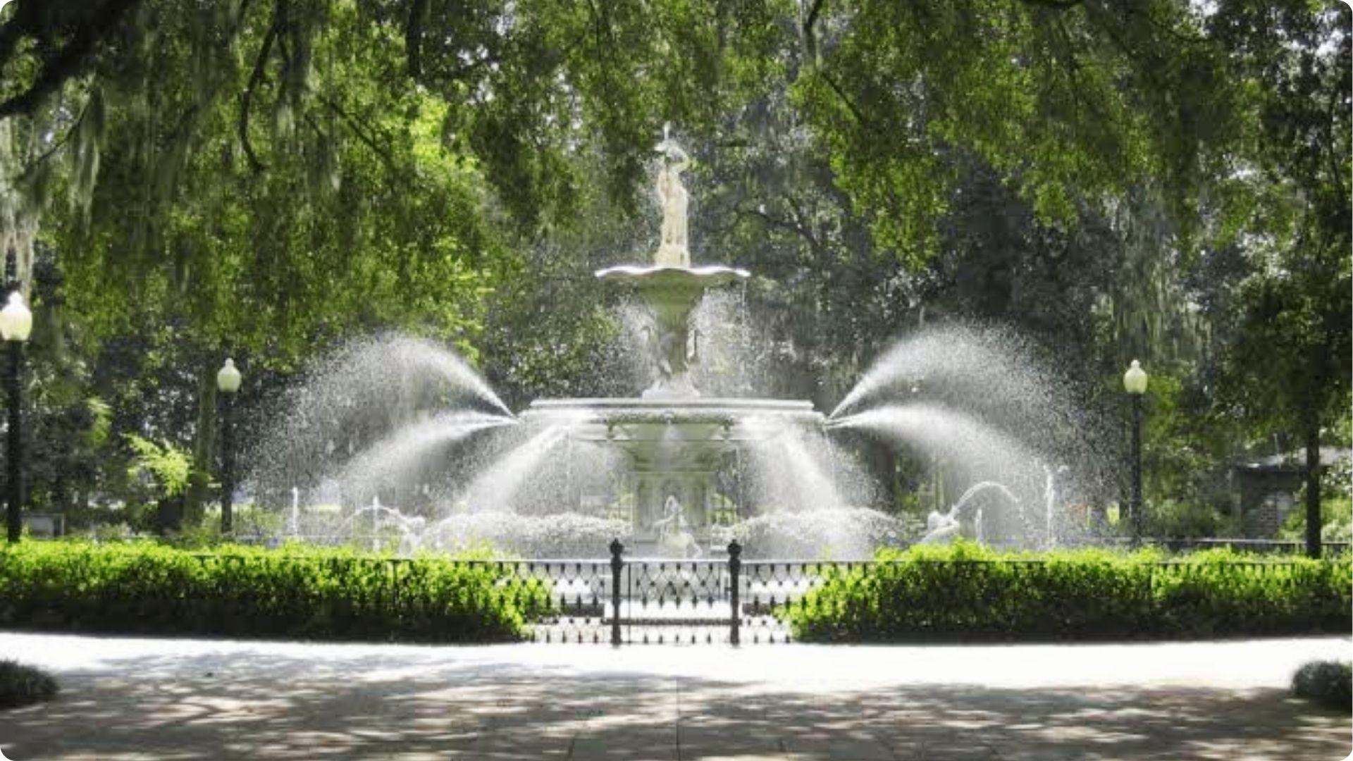 Iconic Forsyth Park fountain spraying water under moss-draped oaks on Savannah walking tour highlight.