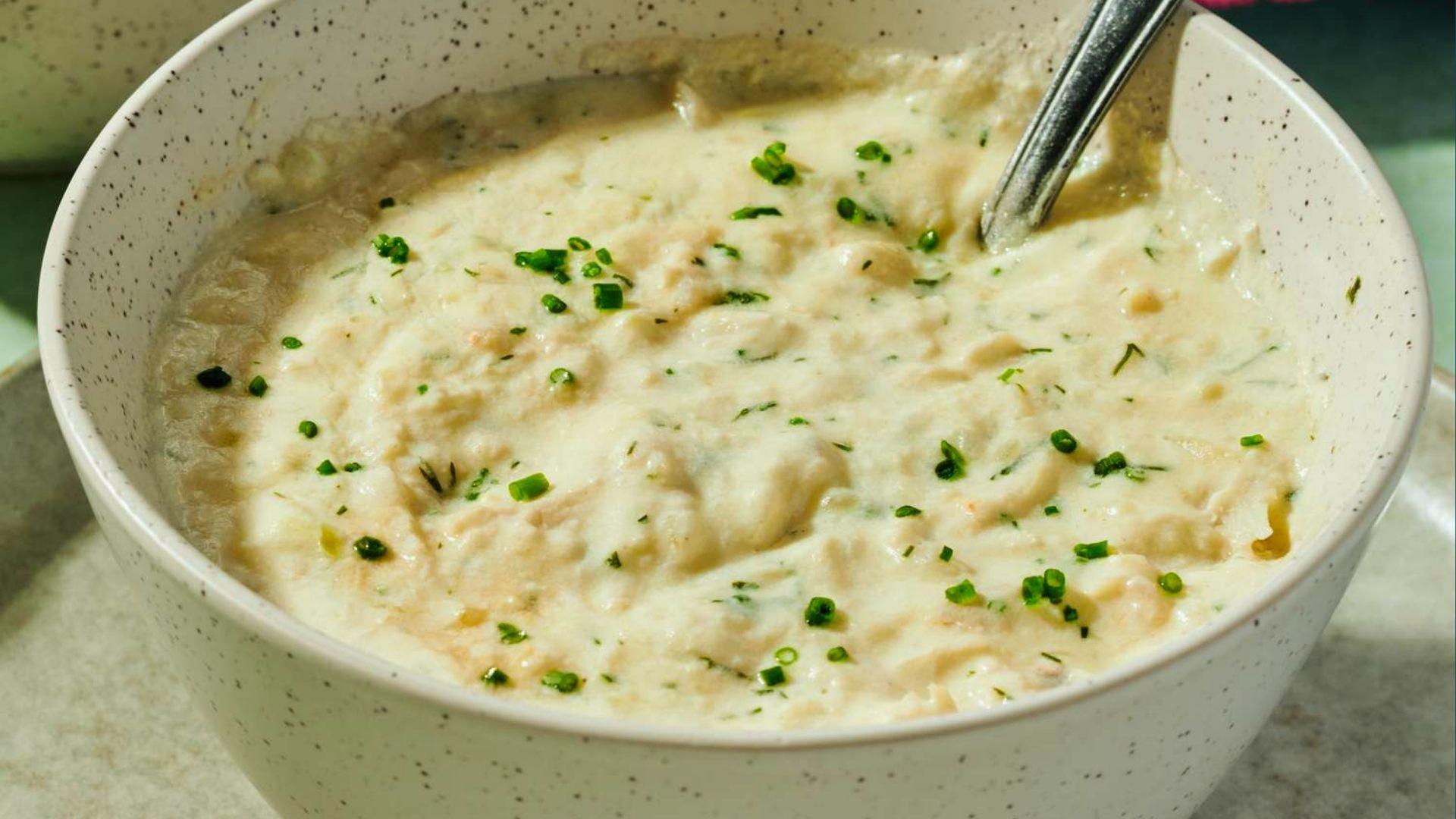 Creamy seafood chowder garnished with chives in speckled bowl with vintage spoon