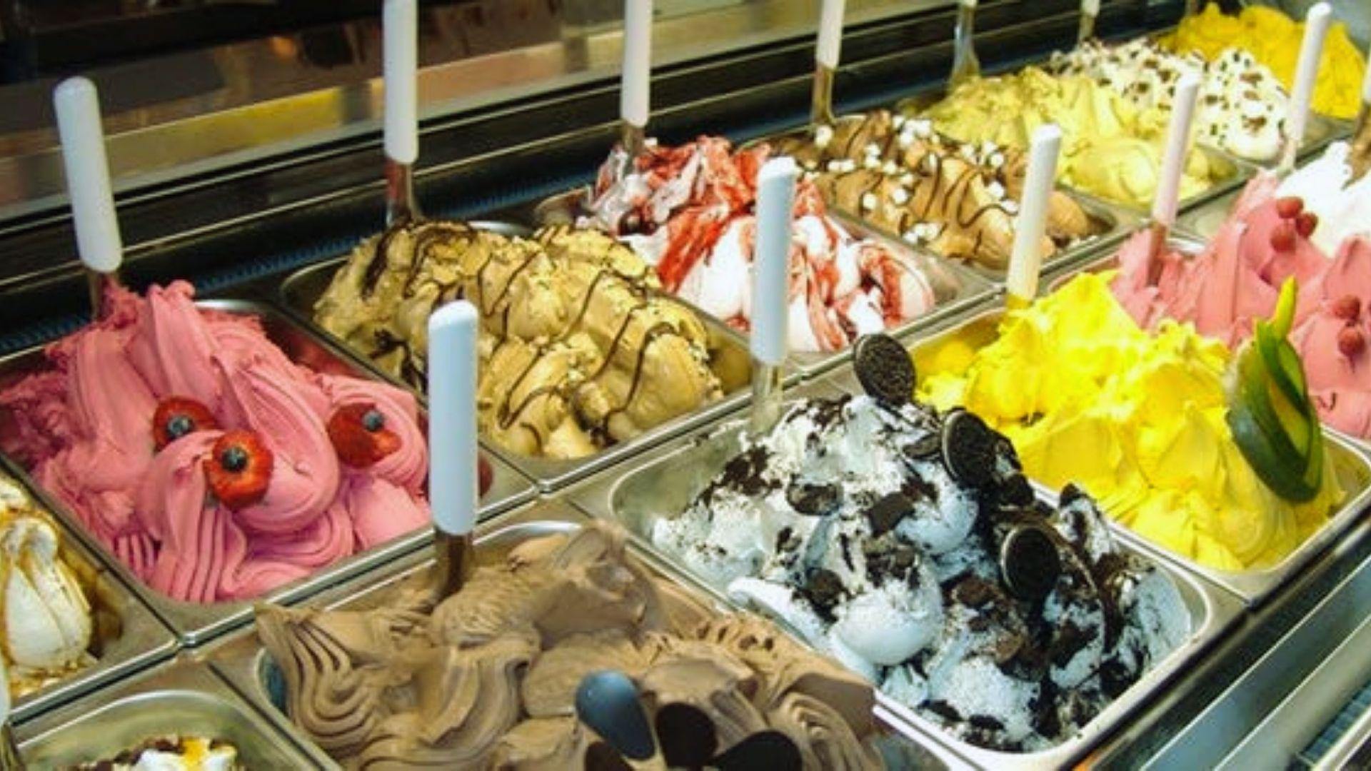 Colorful gelato trays with swirls, cookies, fruit toppings and white scoops in chilled display case
