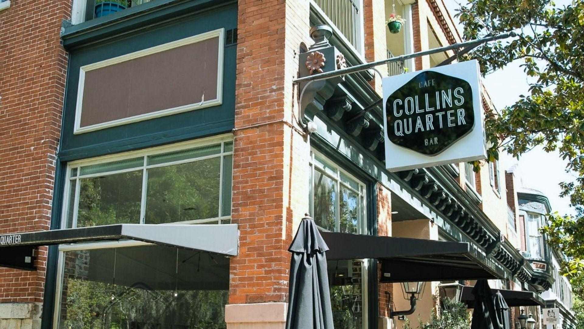 Sunny corner cafe Collins Quarter Bar with outdoor diners at wooden tables, closed black umbrellas, brick building, hanging sign.