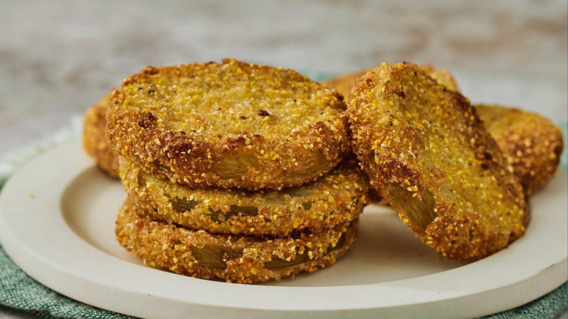 Stacked golden fried green tomatoes with crispy cornmeal crust on white plate