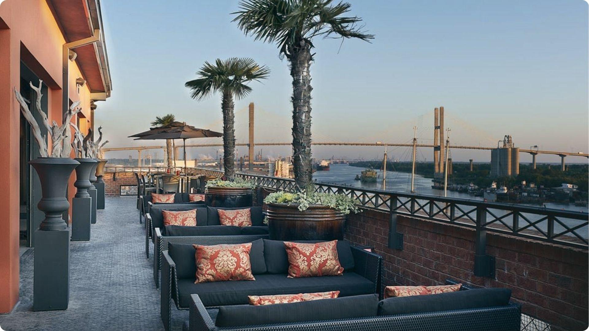 Rooftop happy hour lounge overlooking Savannah River with palm trees and bridge sunset views