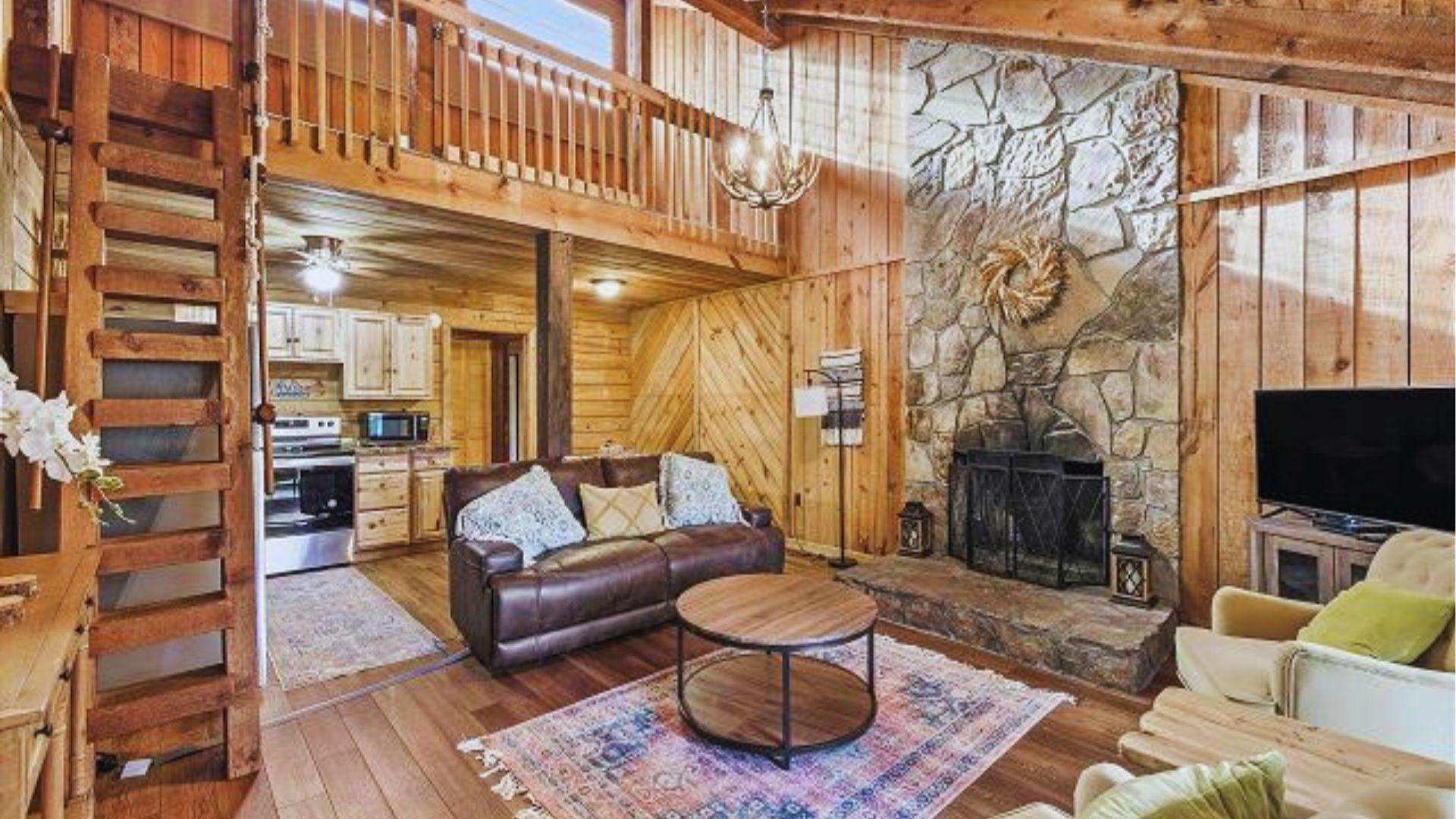 Cozy rustic cabin interior with stone fireplace, leather sofa, wooden loft and warm lighting inside.
