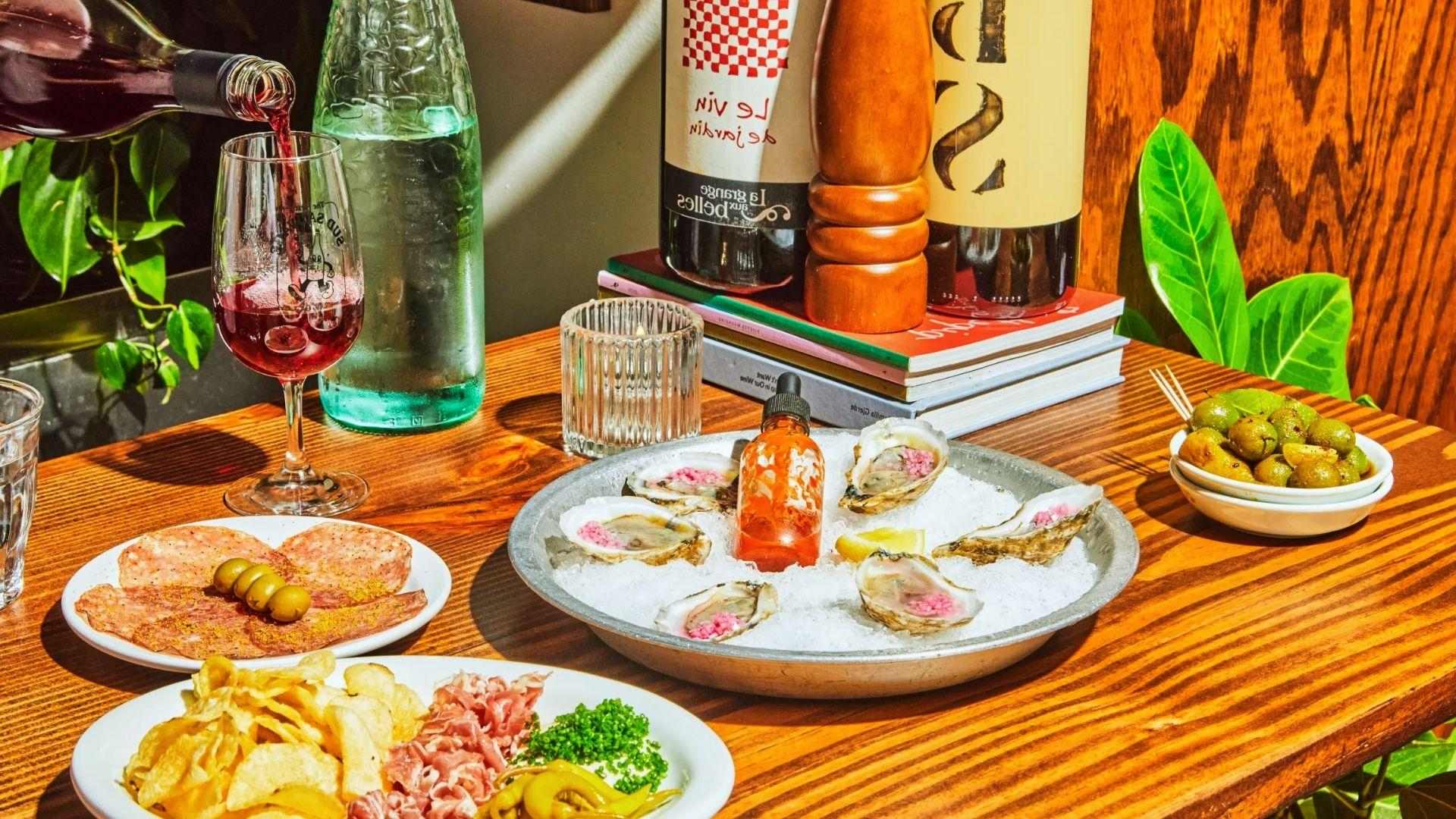 Red wine pouring over oysters, charcuterie and olives on wooden table