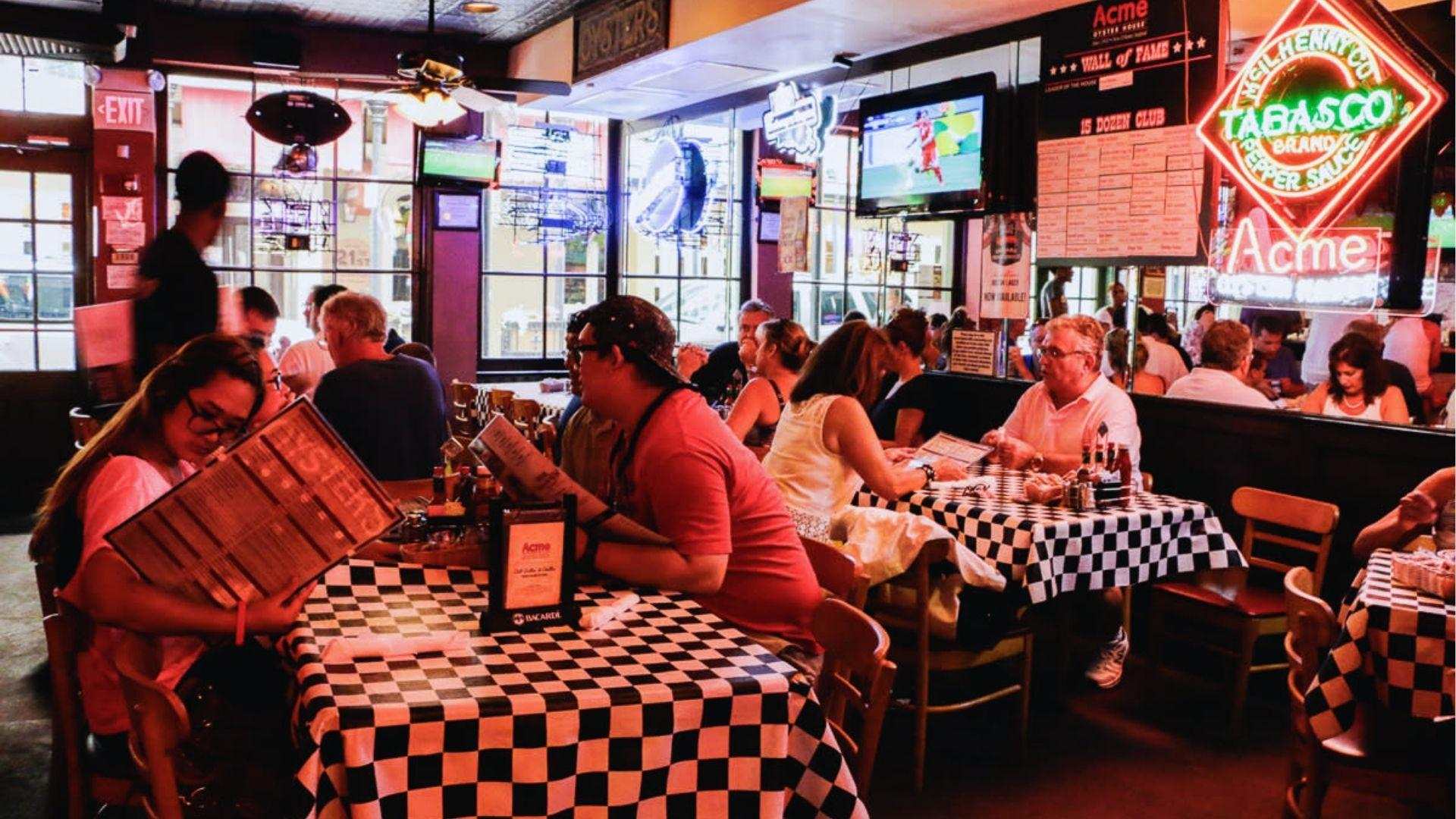 Guests at Acme Oyster House, gathered around tables featuring classic checkered tablecloths, enjoying their dining experience.