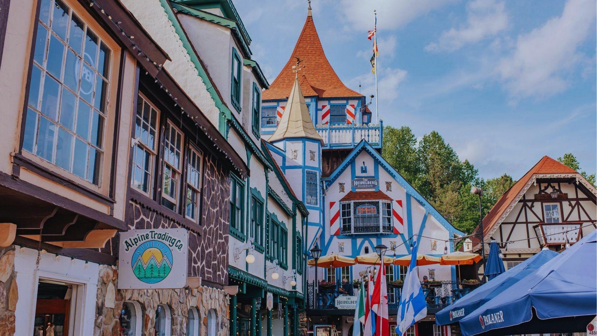 Bavarian street with Alpine Trading Co sign half-timbered buildings flags and blue Paulaner umbrellas outside.