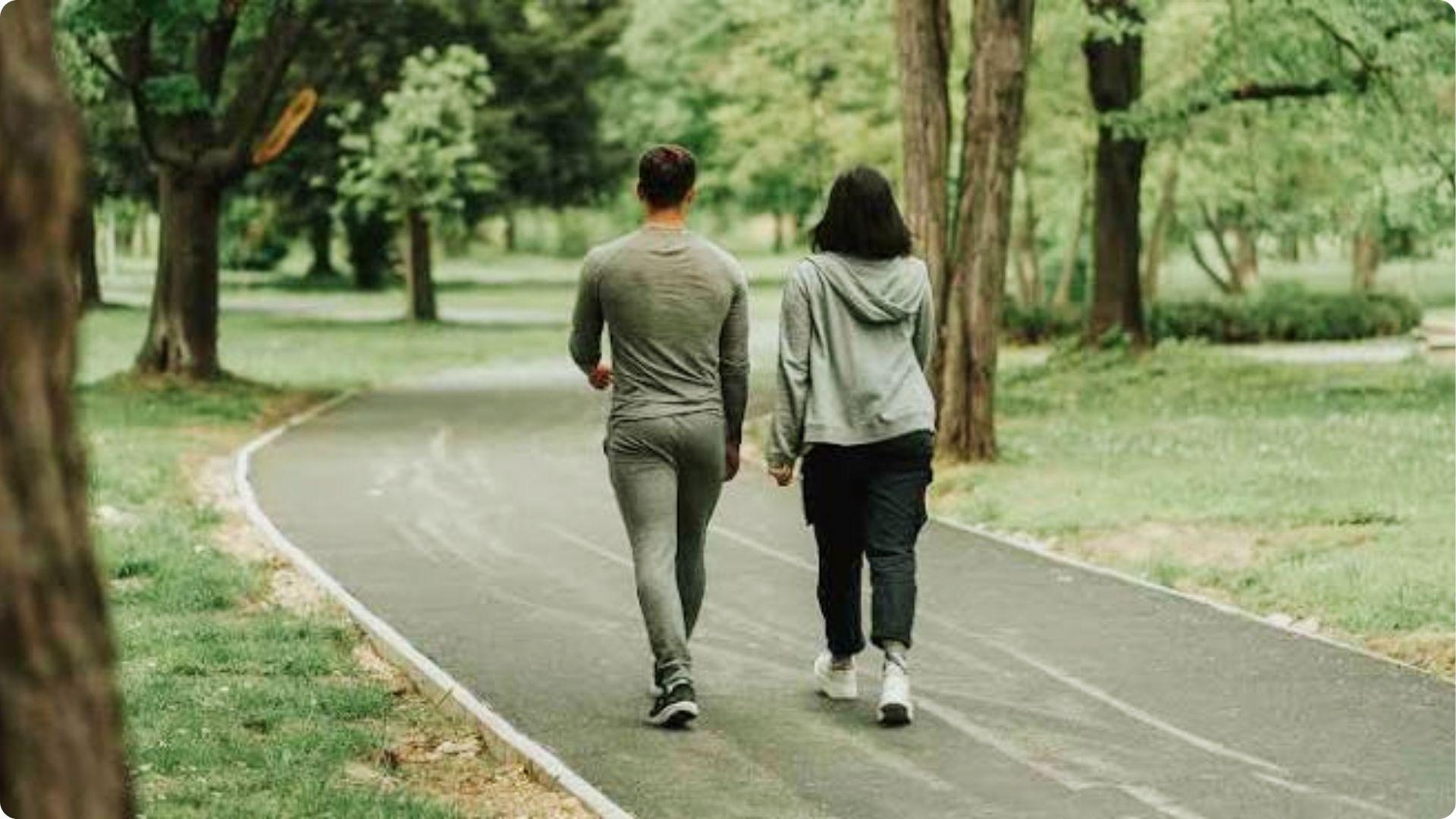 Couple walking hand in hand on shaded park trail surrounded by green trees, Myrtle Beach nature walk
