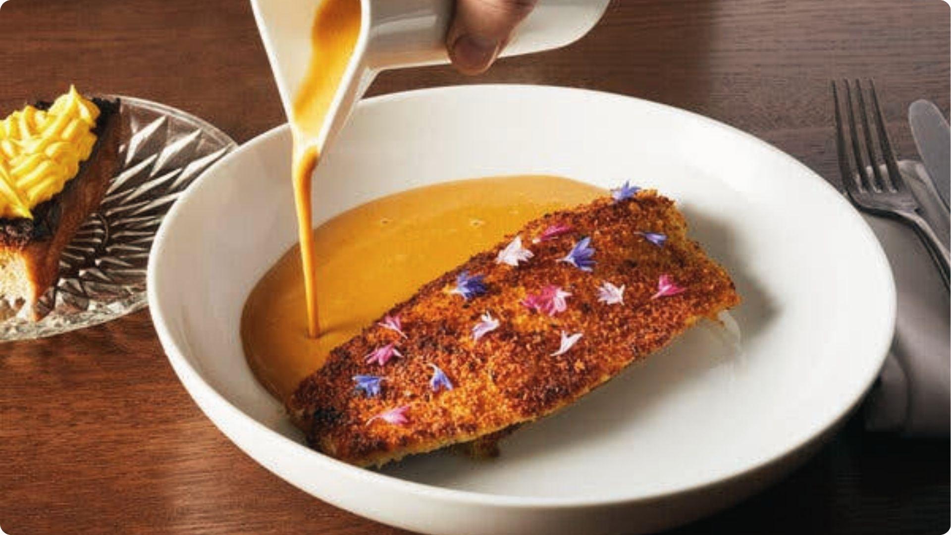 Elegant blackened redfish with edible flowers as creamy Creole sauce pours, fine New Orleans dish.
