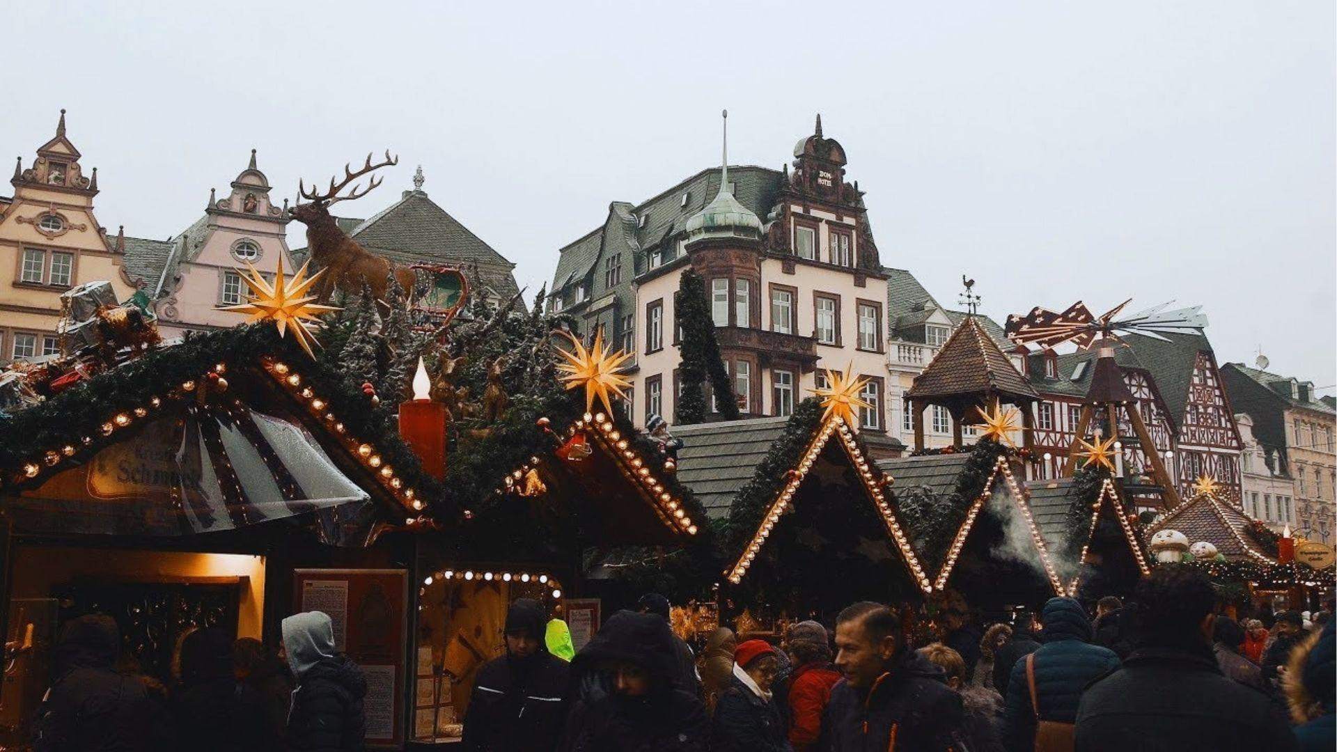European Christmas market with illuminated wooden stalls, star lights, reindeer decoration and historic buildings background.