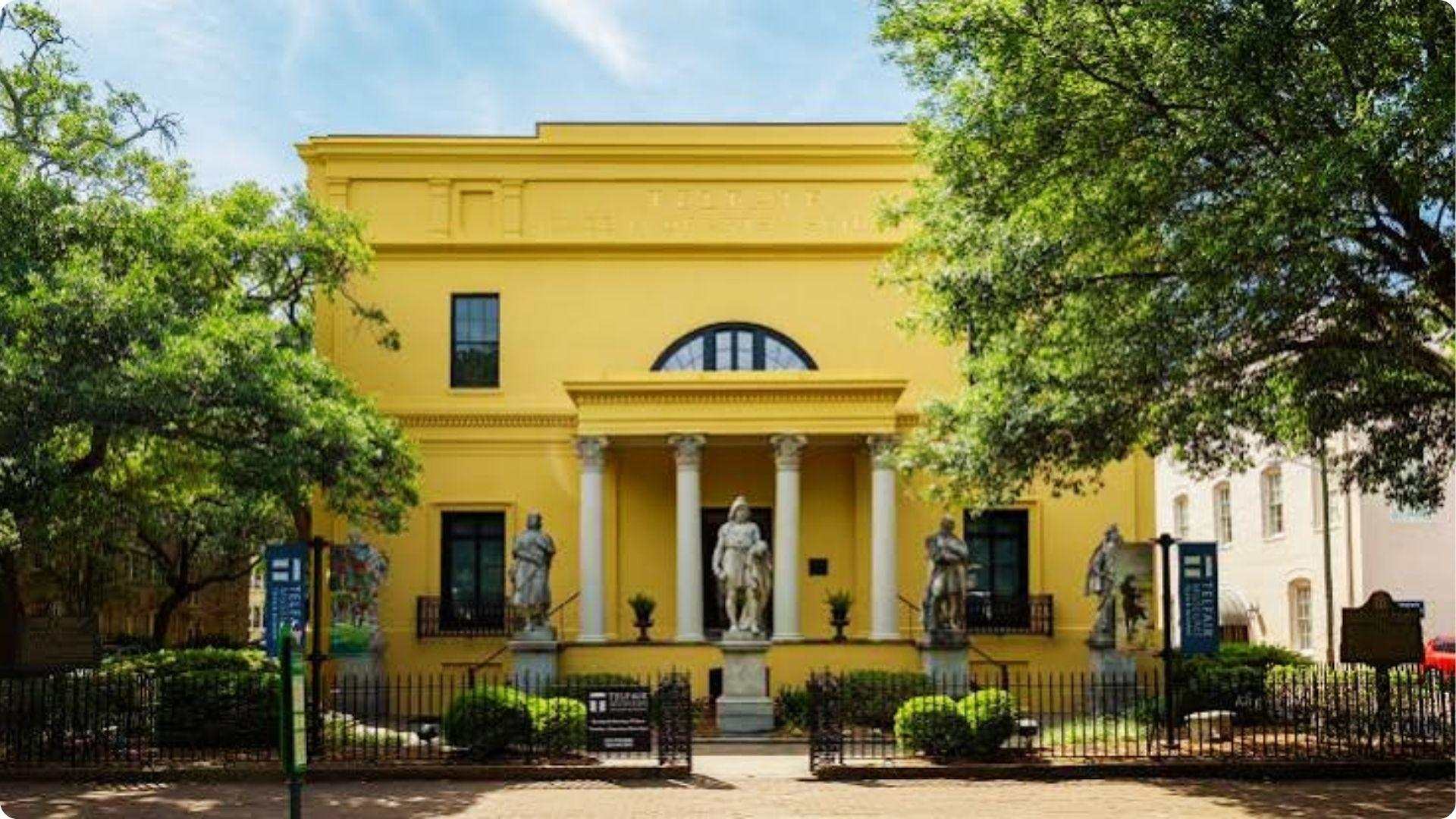 Bright yellow Telfair Academy art museum with statues and oak trees in Savannah Georgia historic