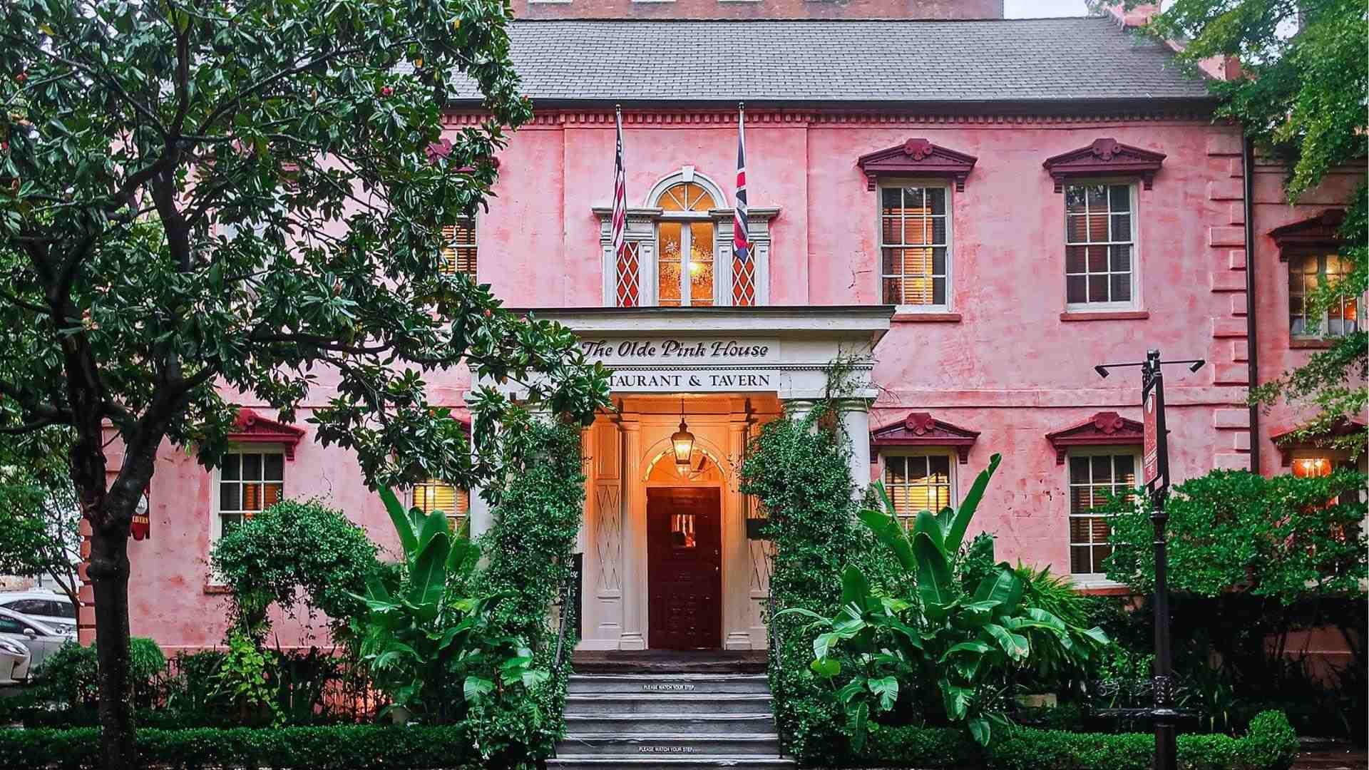 Historic Olde Pink House restaurant facade surrounded by lush greenery and illuminated entrance at dusk.